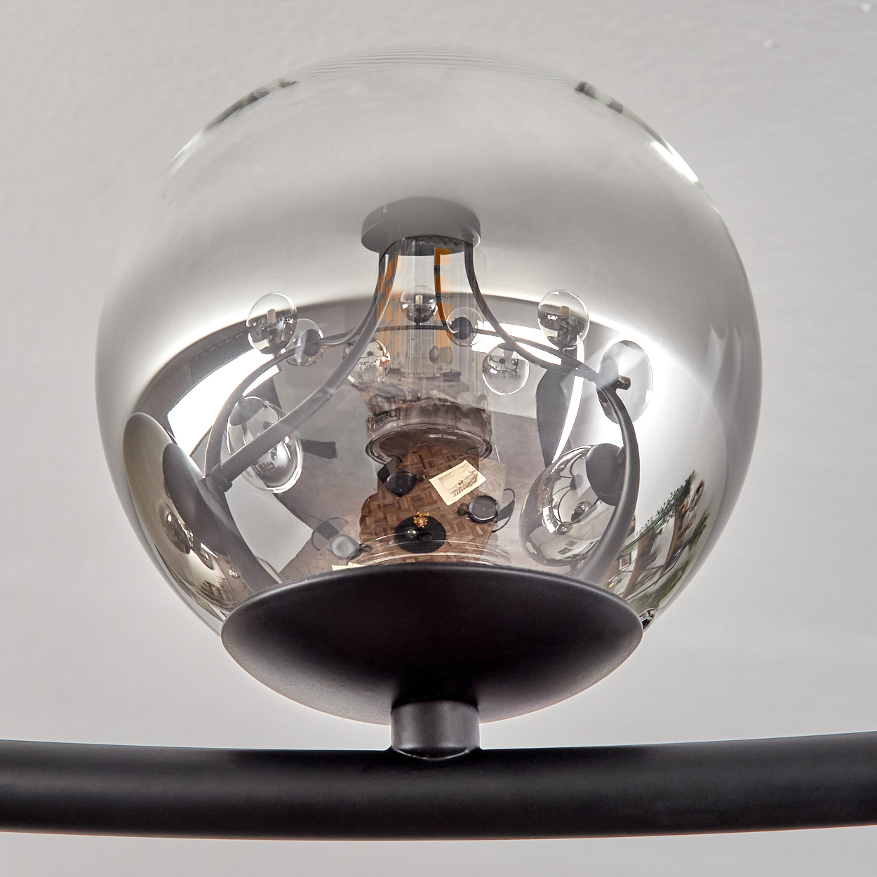 Moderne Leuchte. Eine klare Glaskugel umschließt das Innenleben. Schwarzer Metallsockel und Tragarm. Weißer Hintergrund.