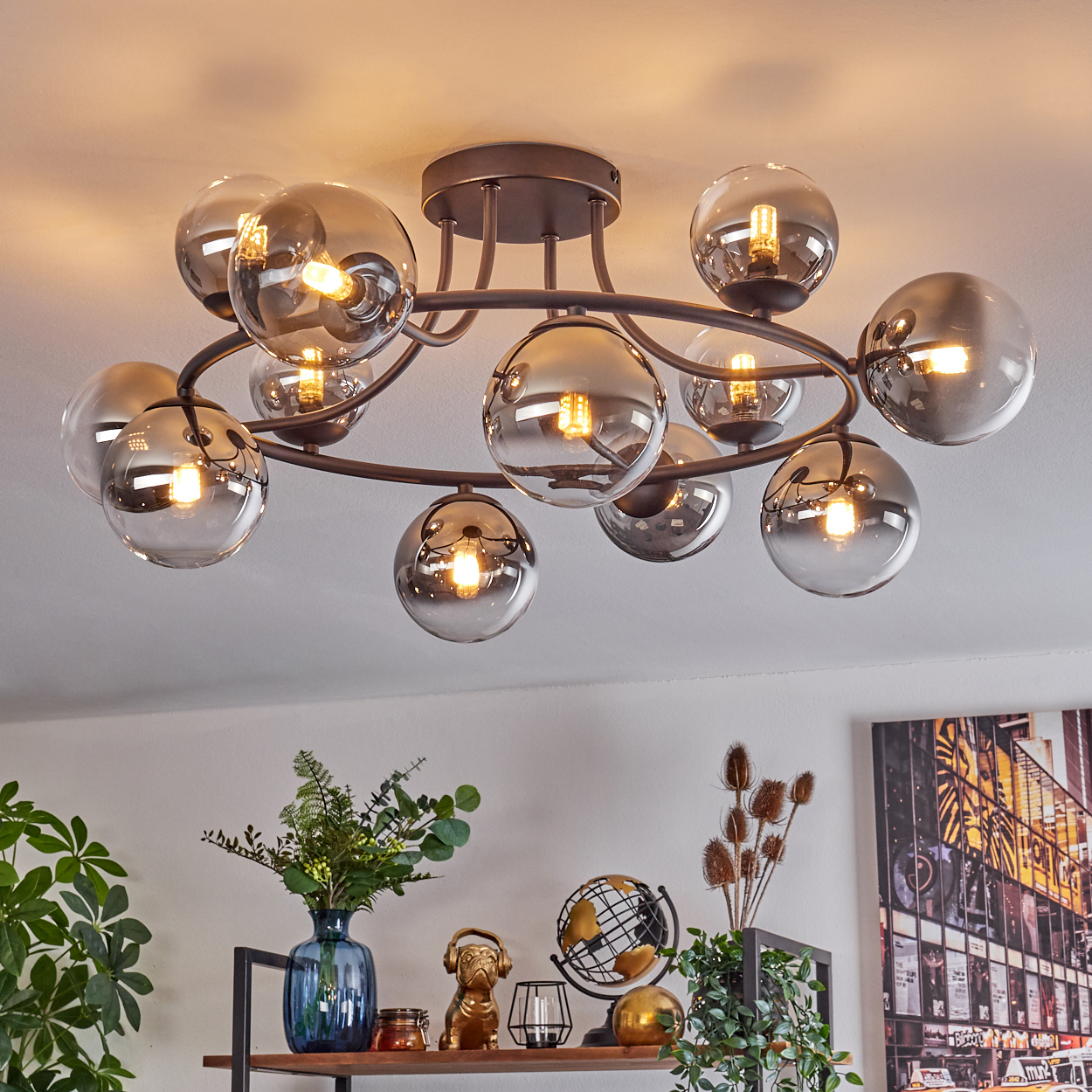 Moderne Deckenleuchte mit Rauchglaskugeln. Darunter ein Regal mit Vase, Globus und anderen Dekorationen. Im Hintergrund eine Wand.
