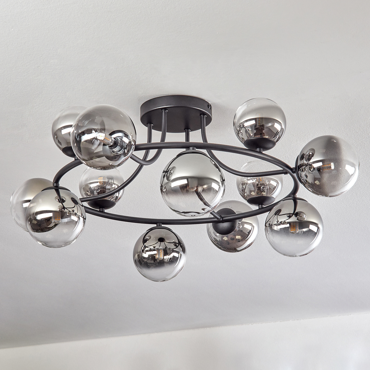 Eine moderne Deckenleuchte mit mehreren reflektierenden Glaskugeln, montiert auf einem schwarzen Metallrahmen, vor einer weißen Decke.