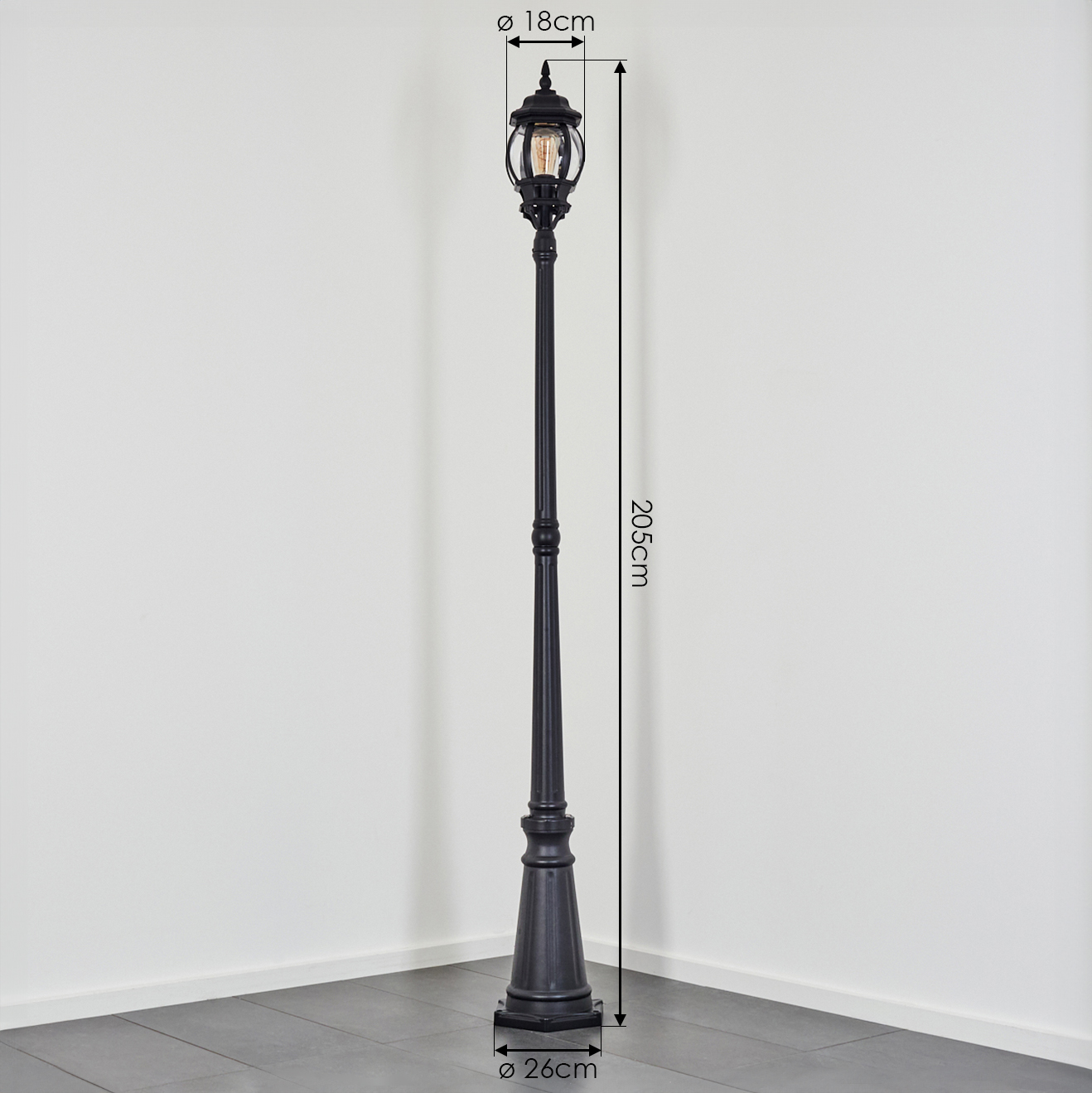 Eine schwarze Vintage-Straßenlaterne steht vor einer weißen Wand und einem grauen Boden. Die Abmessungen sind 18 cm, 205 cm und 26 cm.