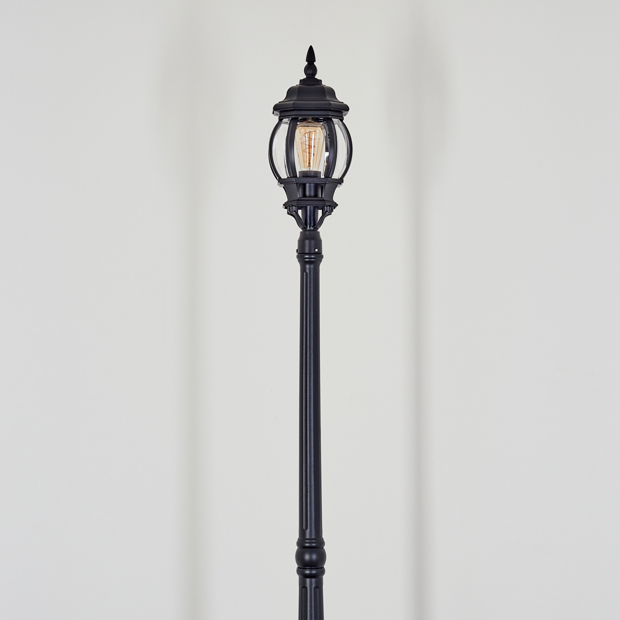 Eine schwarze Vintage-Straßenlaterne vor weißem Hintergrund. Die Lampe hat eine Glaskugel mit sichtbarer Glühbirne.
