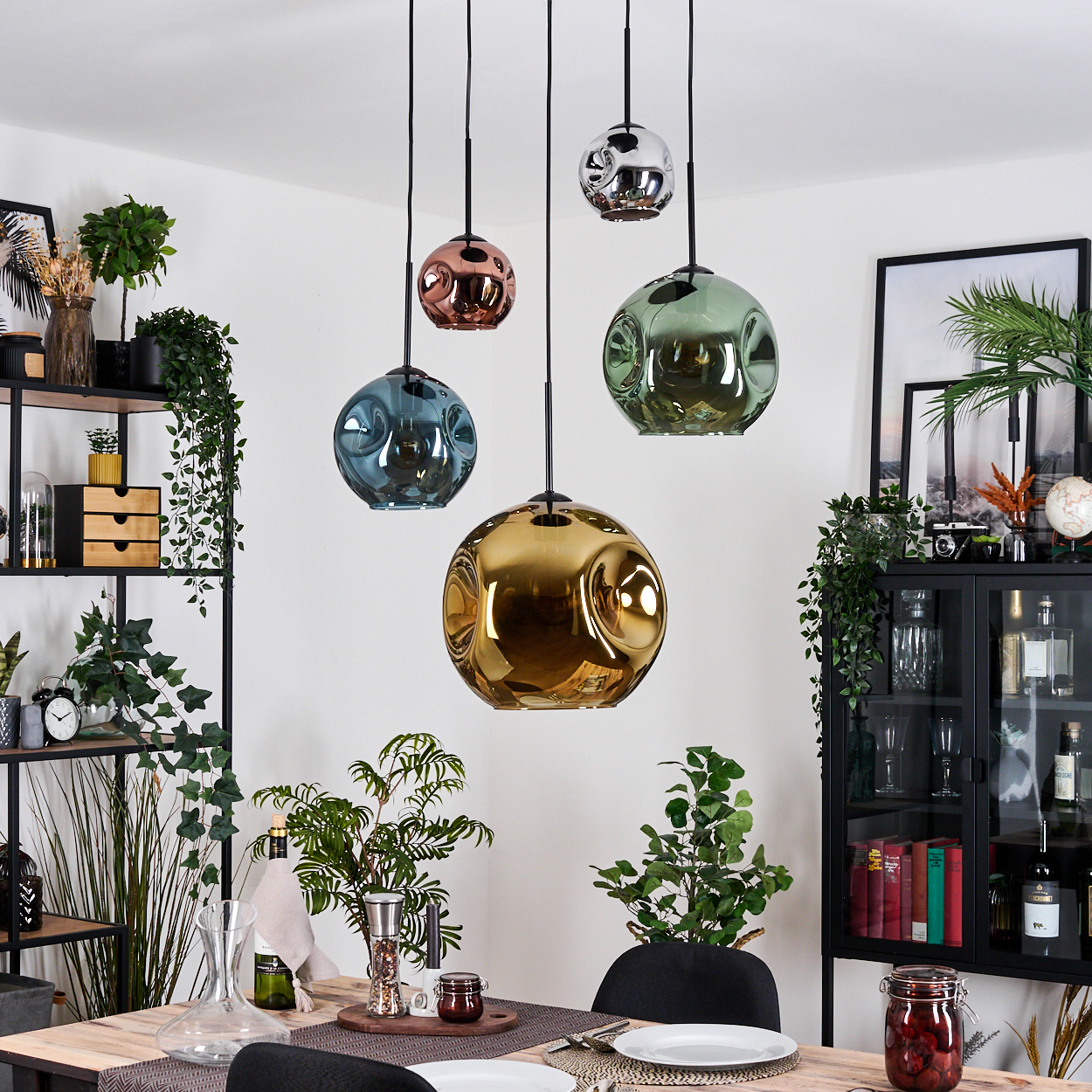 Esszimmer mit hängenden Kugelleuchten in Gold, Blau, Grün, Kupfer und Silber. Pflanzen, Tischgedeck und Regale sind sichtbar.