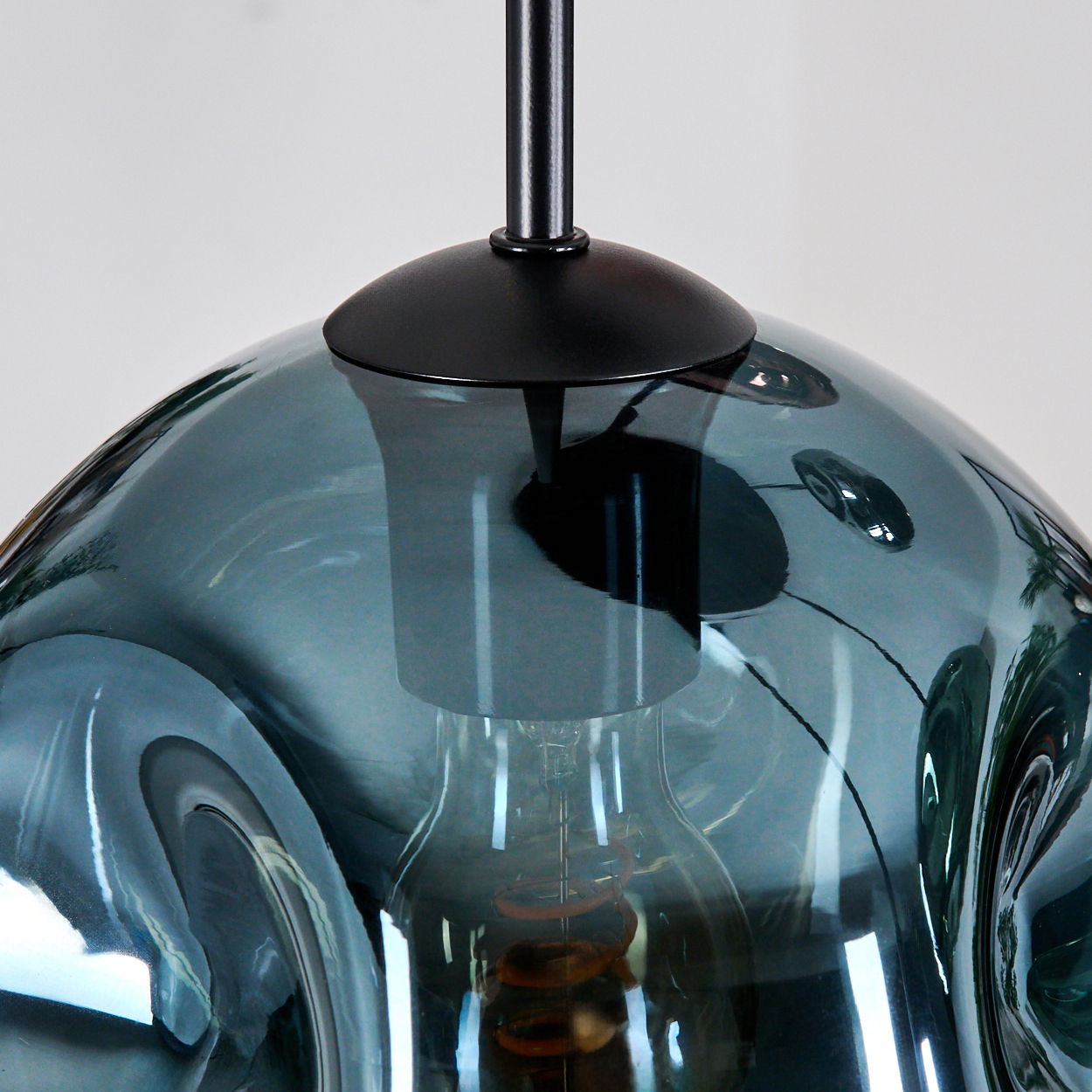 Nahaufnahme einer tealfarbenen Glas-Pendelleuchte mit schwarzem Stiel. Die Glühbirne im Inneren ist sichtbar, der Hintergrund ist weiß.