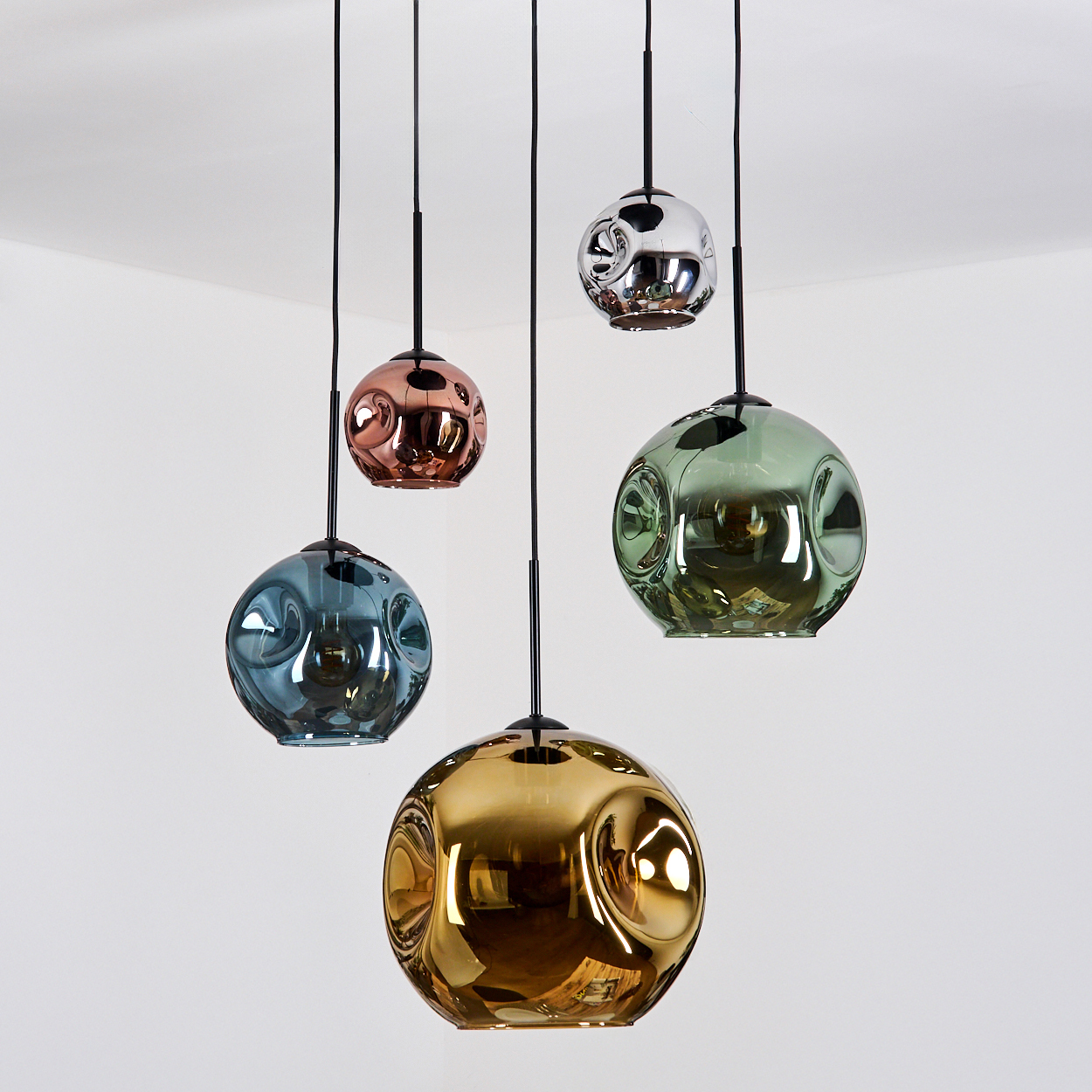 Fünf bunte, kugelförmige Pendelleuchten hängen von der Decke. Farben sind Blau, Kupfer, Grün, Silber und Gold. Weißer Hintergrund.