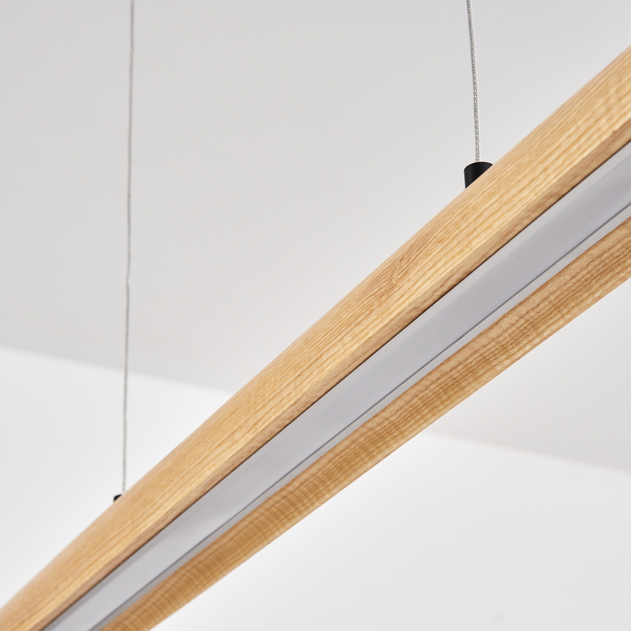 Nahaufnahme eines Holzbalkens mit silbernem Lichtstreifen, der an Drähten vor weißem Hintergrund hängt.