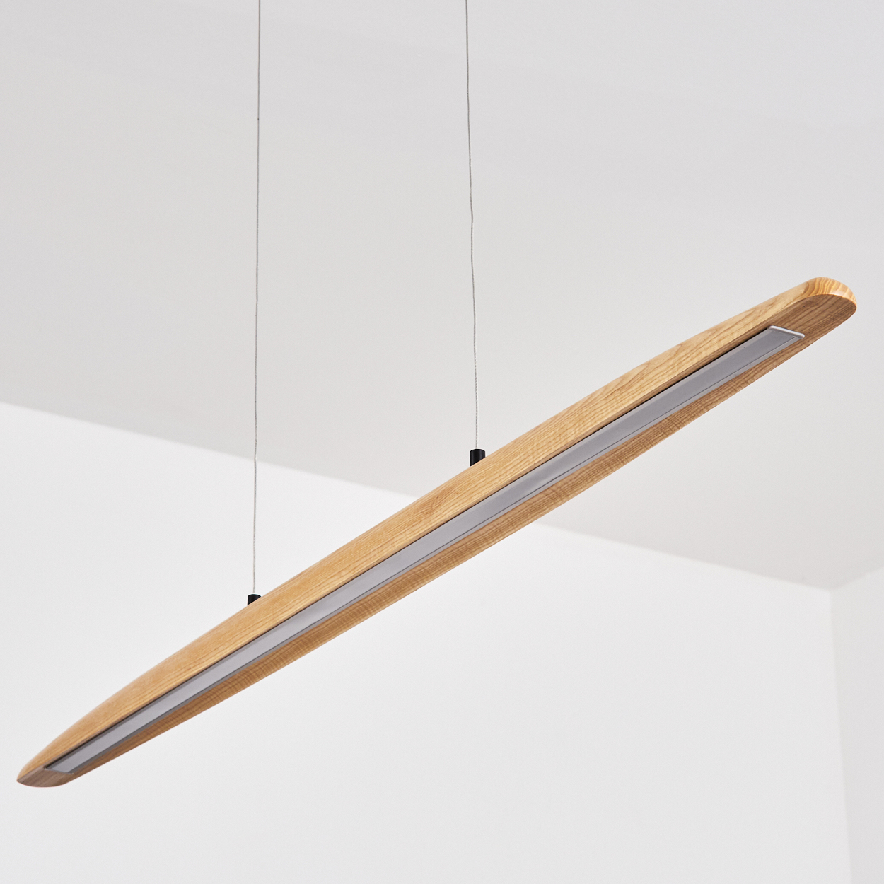 Eine rechteckige Holzleuchte hängt von der Decke. Sie hat einen Metallstreifen in der Mitte und wird von dünnen Drähten gehalten.
