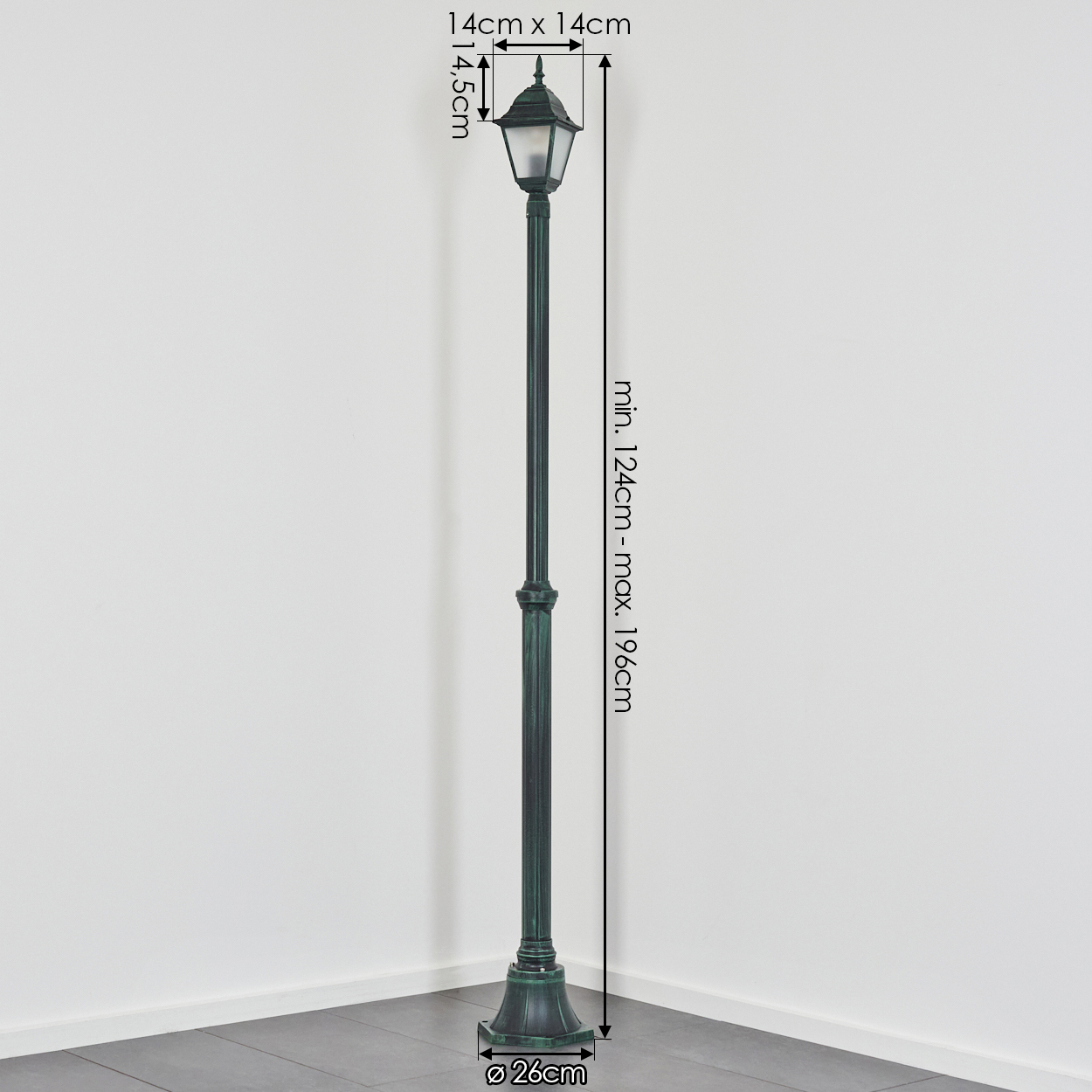 Eine grüne Straßenlaterne steht in einer Ecke vor einer weißen Wand. Maße: Höhe 124-196cm, Oberseite 14x14cm, Sockel Ø 26cm.