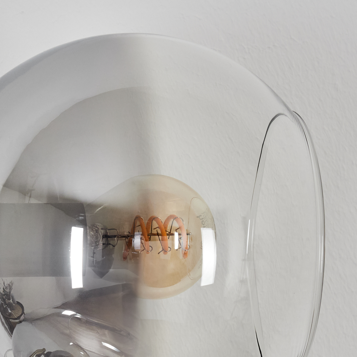 Nahaufnahme einer Glühbirne in einer transparenten Glaskugel. Der Glühfaden der Birne ist eine Spirale aus Orange. Der Hintergrund ist weiß.