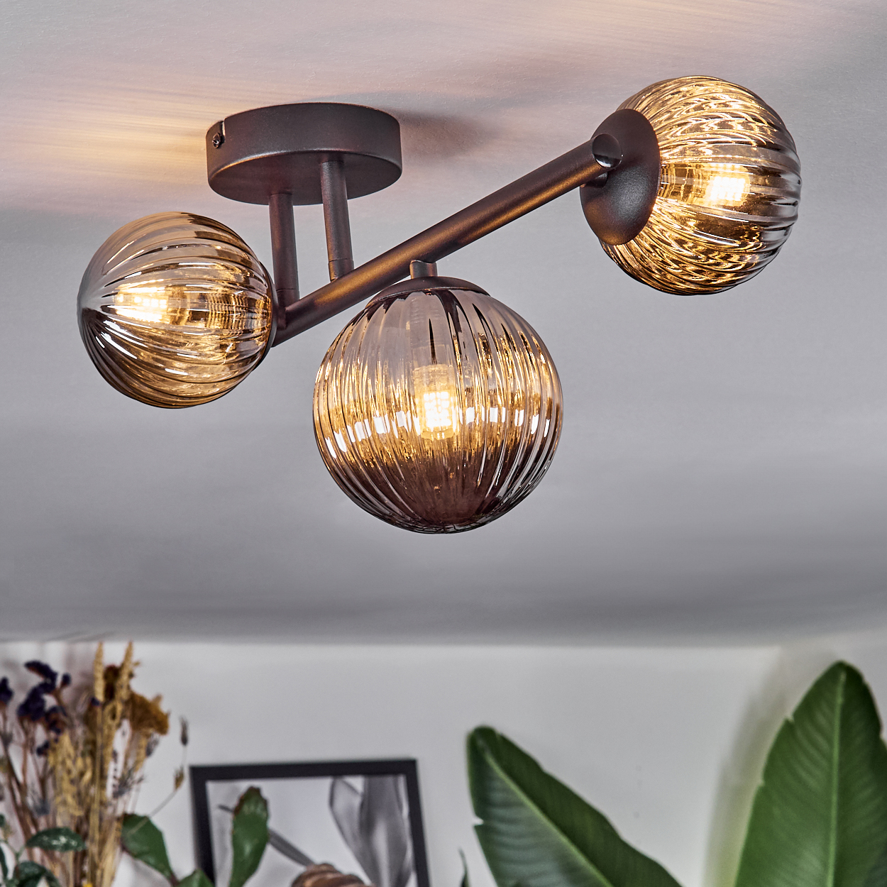 Eine moderne Deckenleuchte mit drei Glaskugel-Schirmen. Die Schirme sind gerippt und strahlen warmes Licht aus. Das Gestell ist dunkles Metall.
