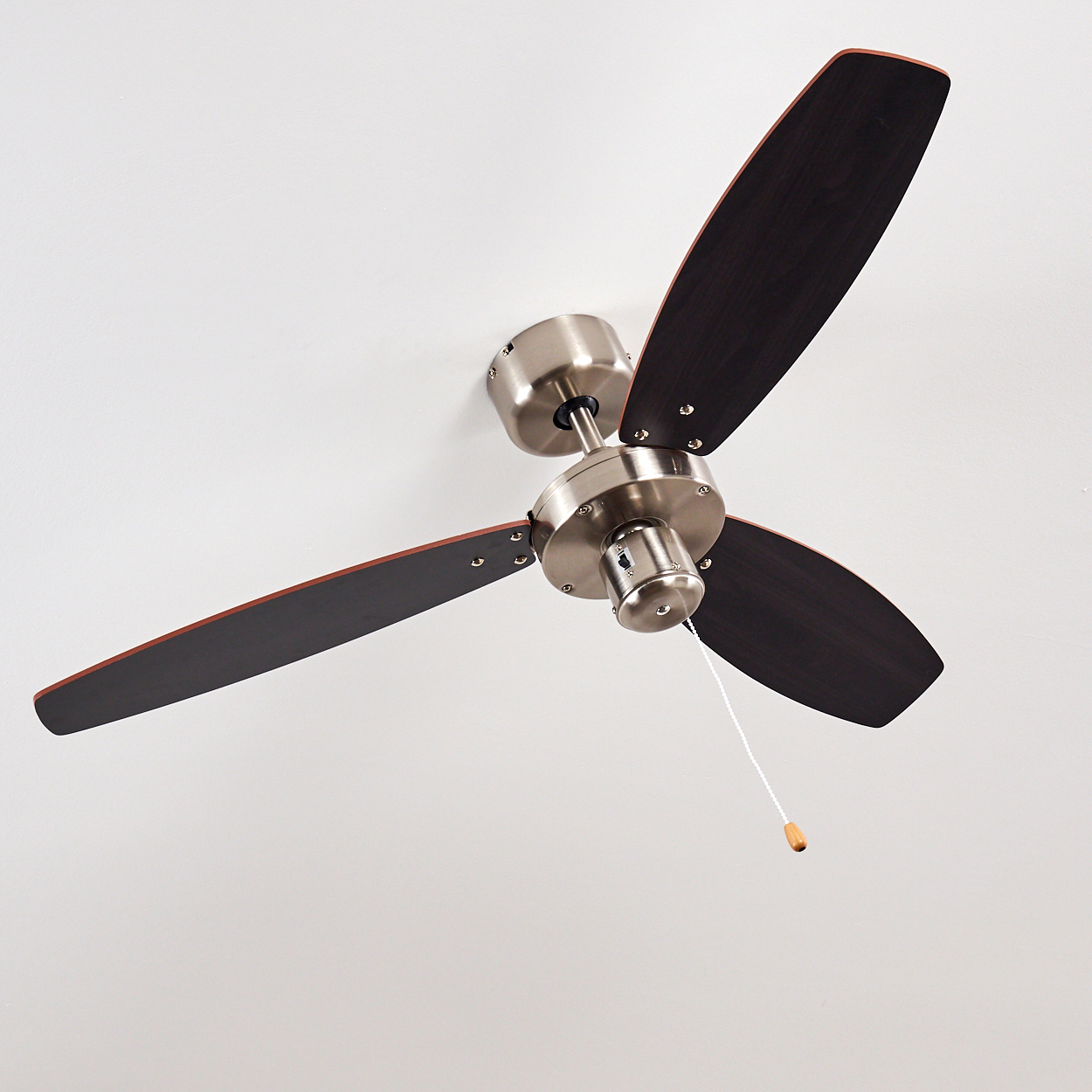 Deckenventilator mit drei dunkelbraunen Flügeln und gebürstetem Nickel-Finish. Er hat eine Zugkette und ist an einer weißen Decke montiert.