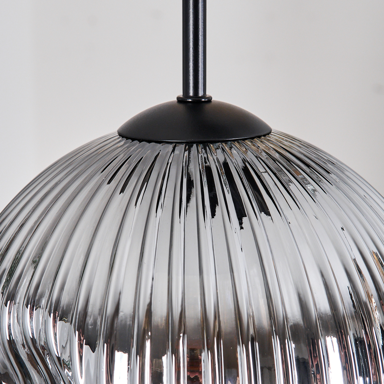 Nahaufnahme einer silbernen, gerippten Glas-Pendelleuchte. Die Lampe hat einen schwarzen Metallsockel und -schaft vor weißem Hintergrund.