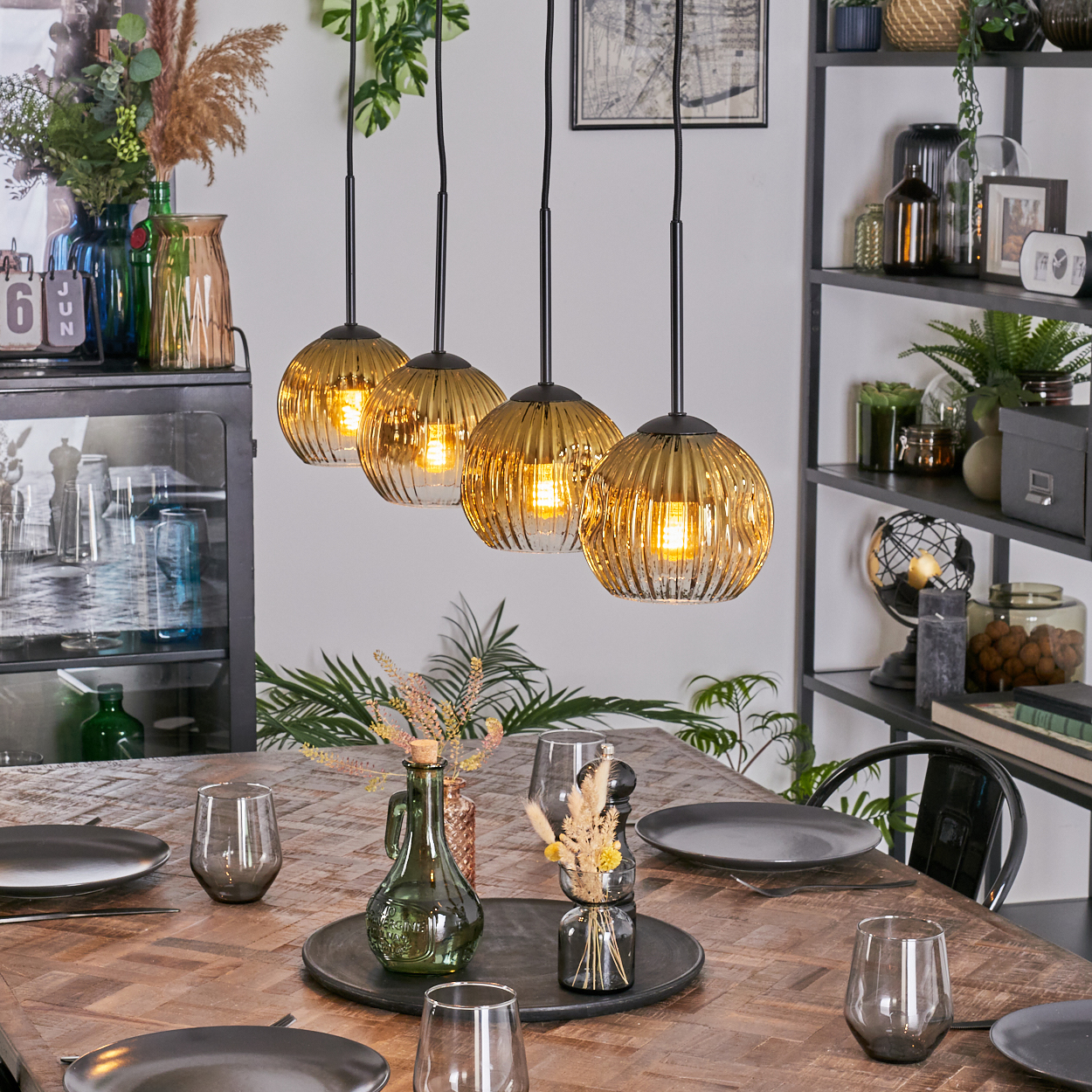 Esszimmer-Szene mit einem Holztisch, der für das Abendessen gedeckt ist. Vier goldene Pendelleuchten hängen darüber. Regale mit Dekoration sind im Hintergrund.