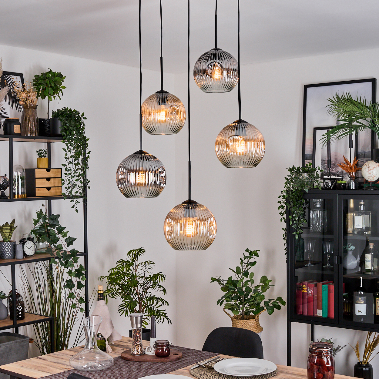 Esszimmer mit hängenden Kugelleuchten. Tisch mit Pflanzen und Dekoration. Regale mit Pflanzen und Dekoration. Schwarzer Schrank.