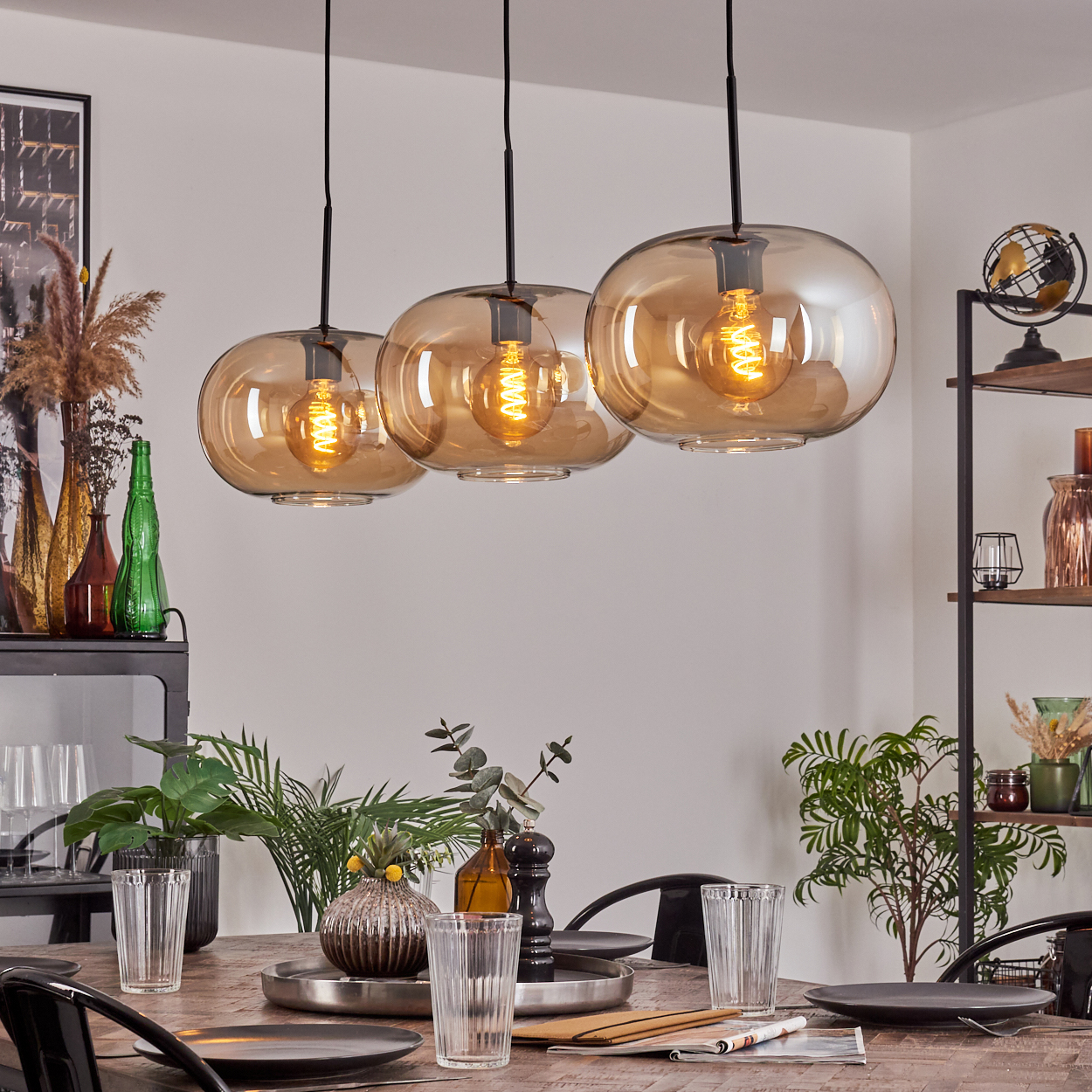 Esszimmer mit Holztisch, gedeckt mit Tellern, Gläsern und Dekorationen. Drei Hängelampen über dem Tisch.