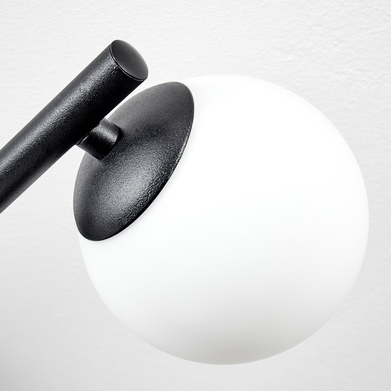 Nahaufnahme einer modernen Lampe. Sie hat einen schwarzen Arm und einen weißen, kugelförmigen Lampenschirm auf weißem Hintergrund.