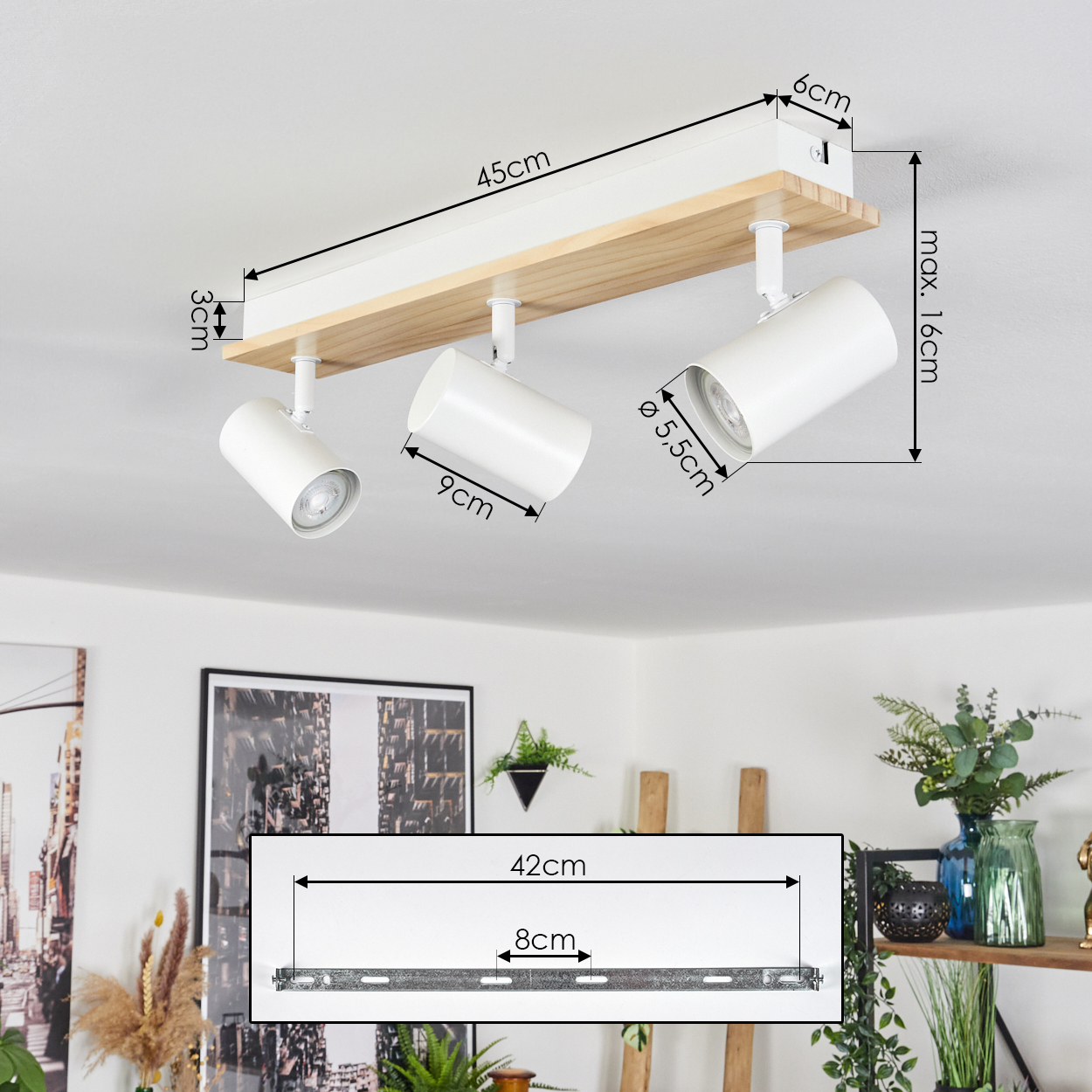 Weißer Deckenstrahler mit drei Lampen, montiert auf Holz und Weiß, Maße sind angegeben. Hintergrund zeigt Dekoration.