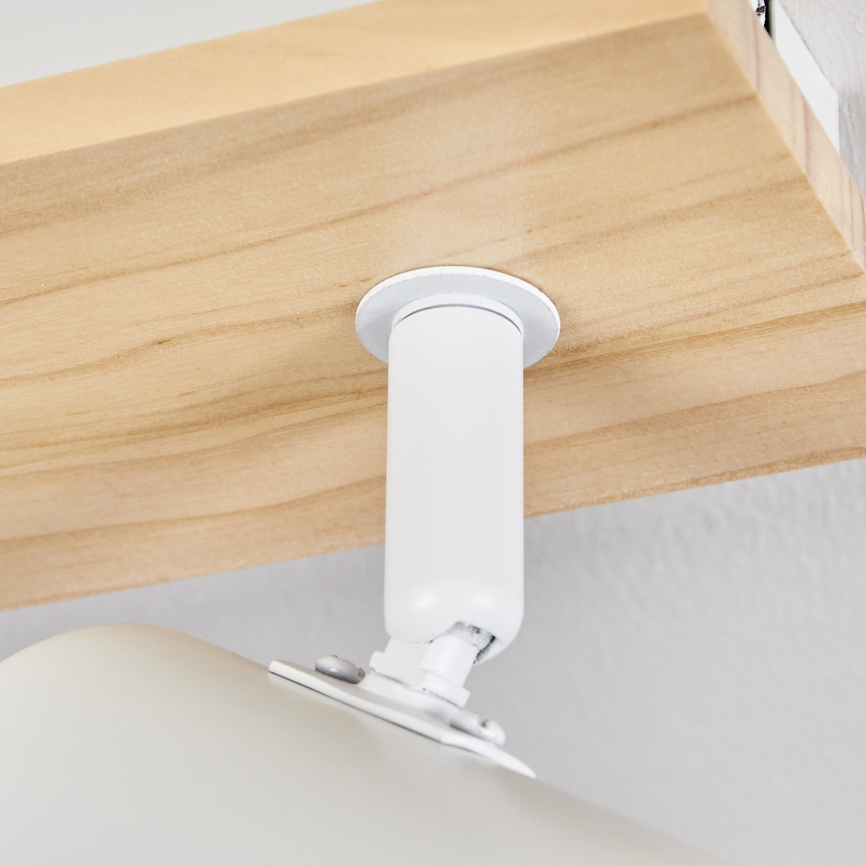 Eine weiße Lampe ist an einem Holzregal befestigt. Die Lampe hat einen zylindrischen Körper und ist abgewinkelt. Das Regal ist hellbraun.