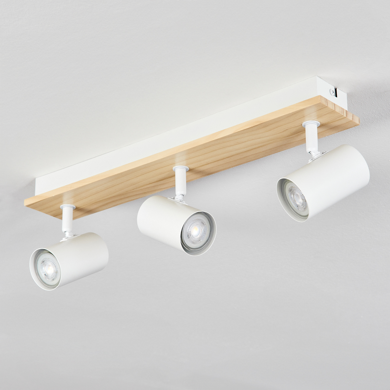 Drei weiße Strahler, montiert auf einem Holzbalken, der an einer weißen Decke befestigt ist. Die Lichter zeigen nach unten.