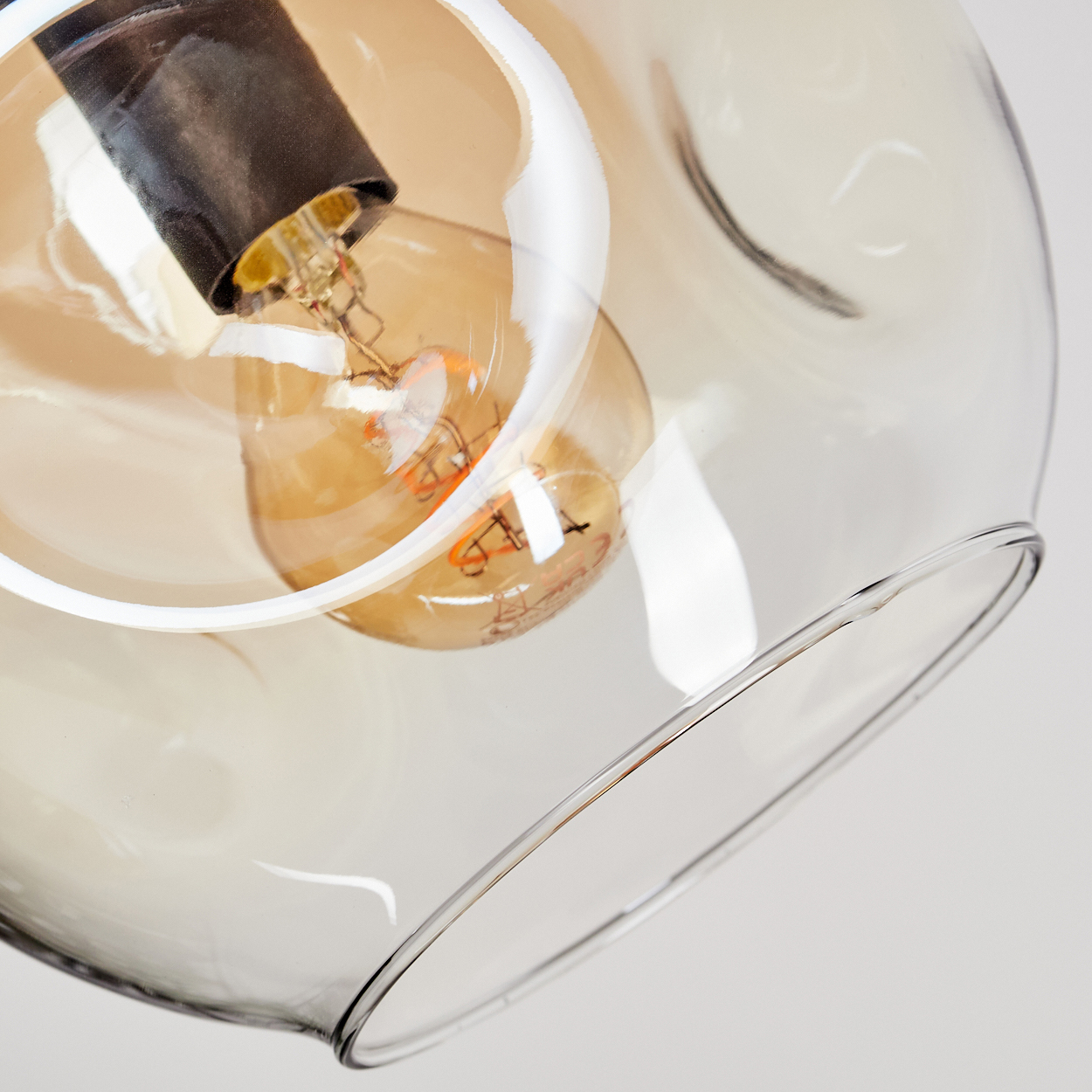 Nahaufnahme einer Glasleuchte. Ein klarer, runder Glasschirm umgibt eine Glühbirne. Die Glühbirne leuchtet, ihre orangefarbenen Filamente sind sichtbar.