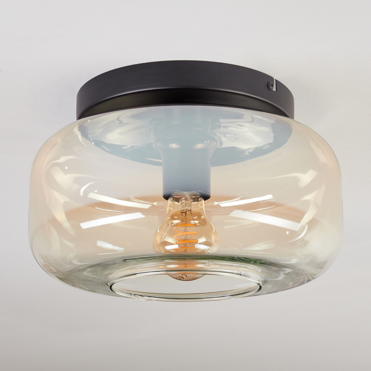 Eine moderne Deckenlampe mit schwarzem Sockel, Glasschirm und sichtbarer Glühbirne. Die Glühbirne leuchtet.
