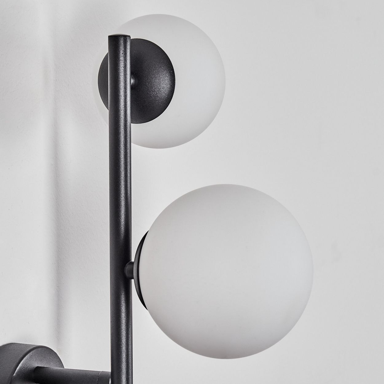 Eine moderne Wandlampe mit zwei weißen Kugelschirmen und einem schwarzen Metallrahmen an einer weißen Wand.