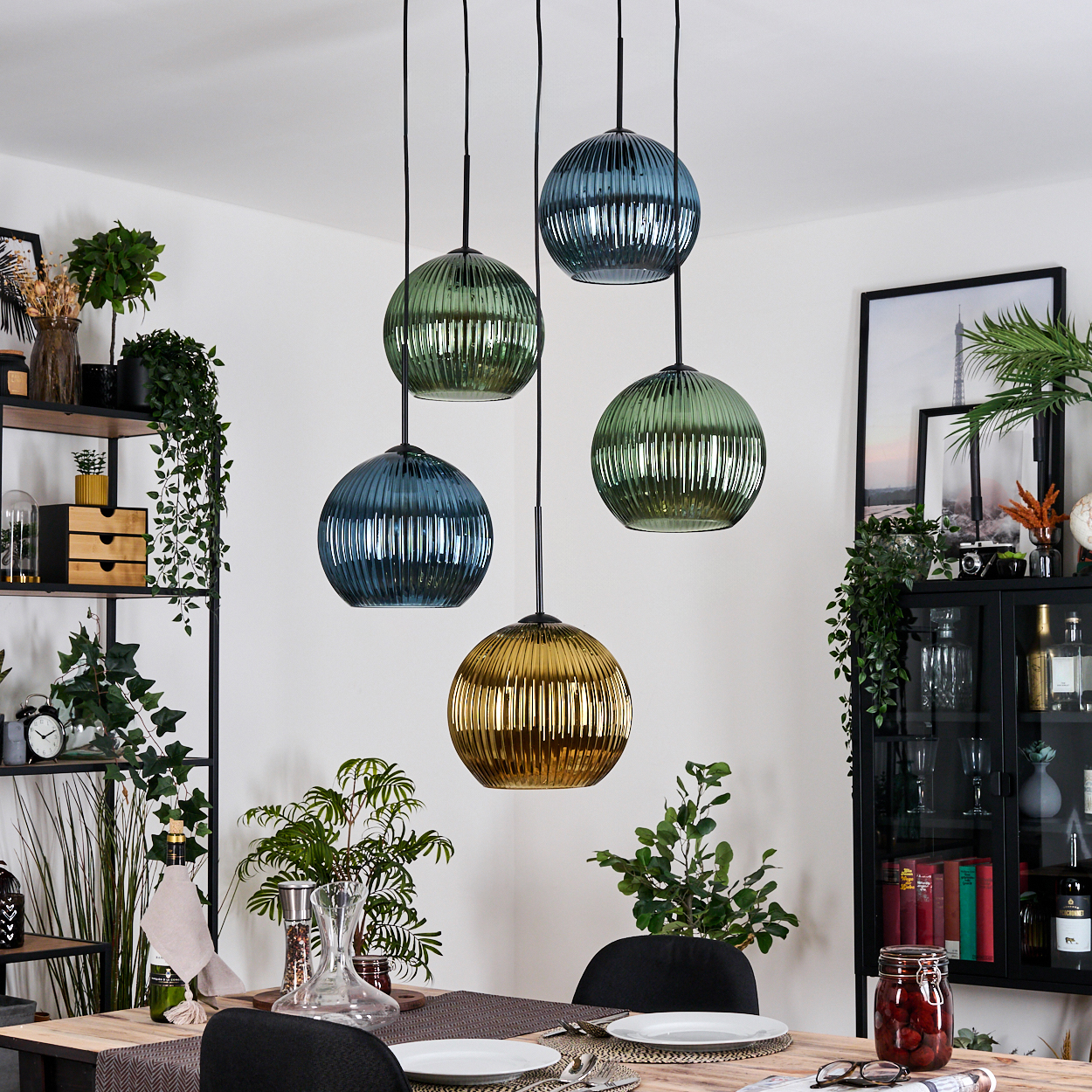 Esszimmer mit hängenden Kugelleuchten in Blau und Grün. Tisch mit Tellern und Gläsern. Regale mit Dekoration.
