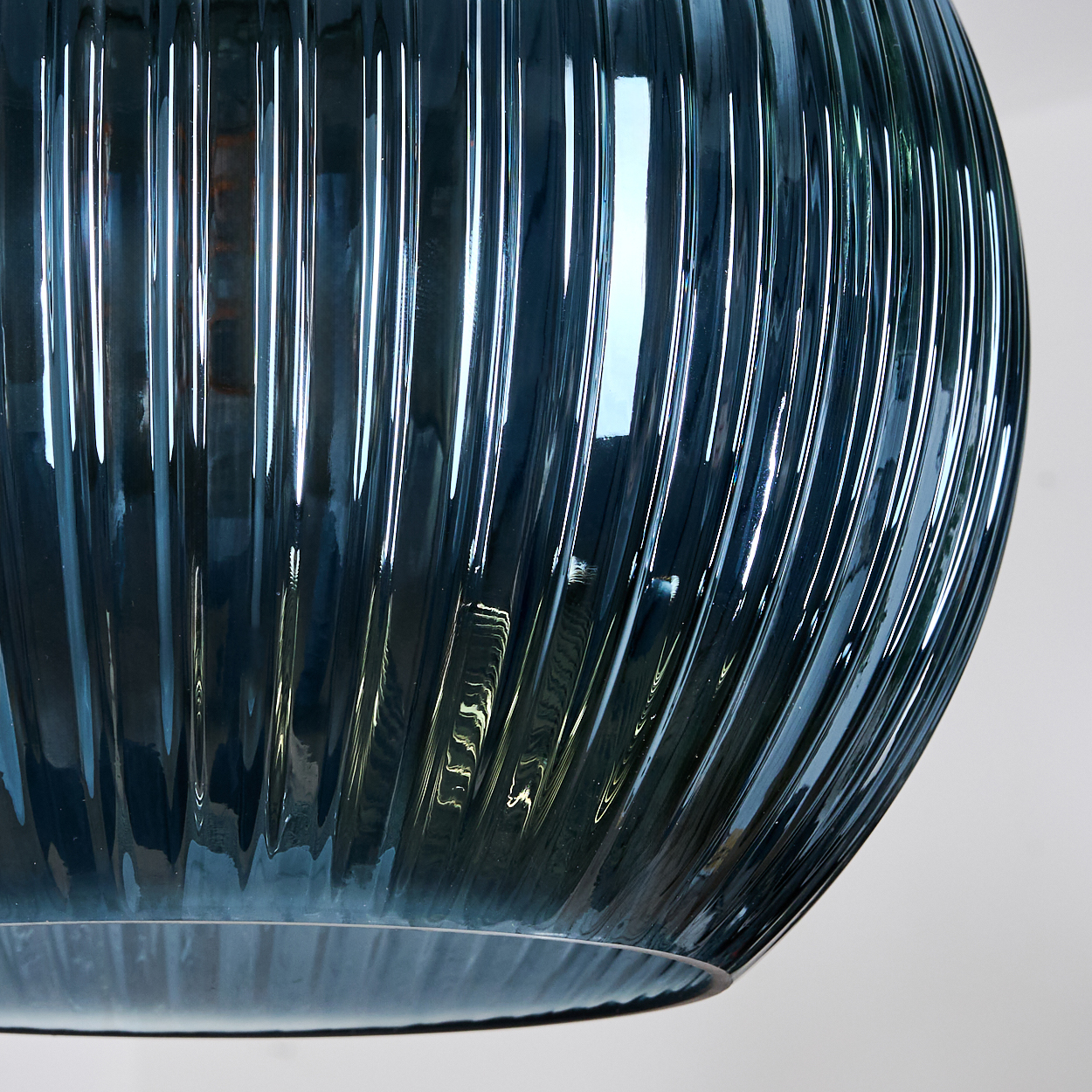 Nahaufnahme eines blauen Glasobjekts mit vertikalen Rippen. Licht reflektiert von der Oberfläche. Der Hintergrund ist schlicht weiß.
