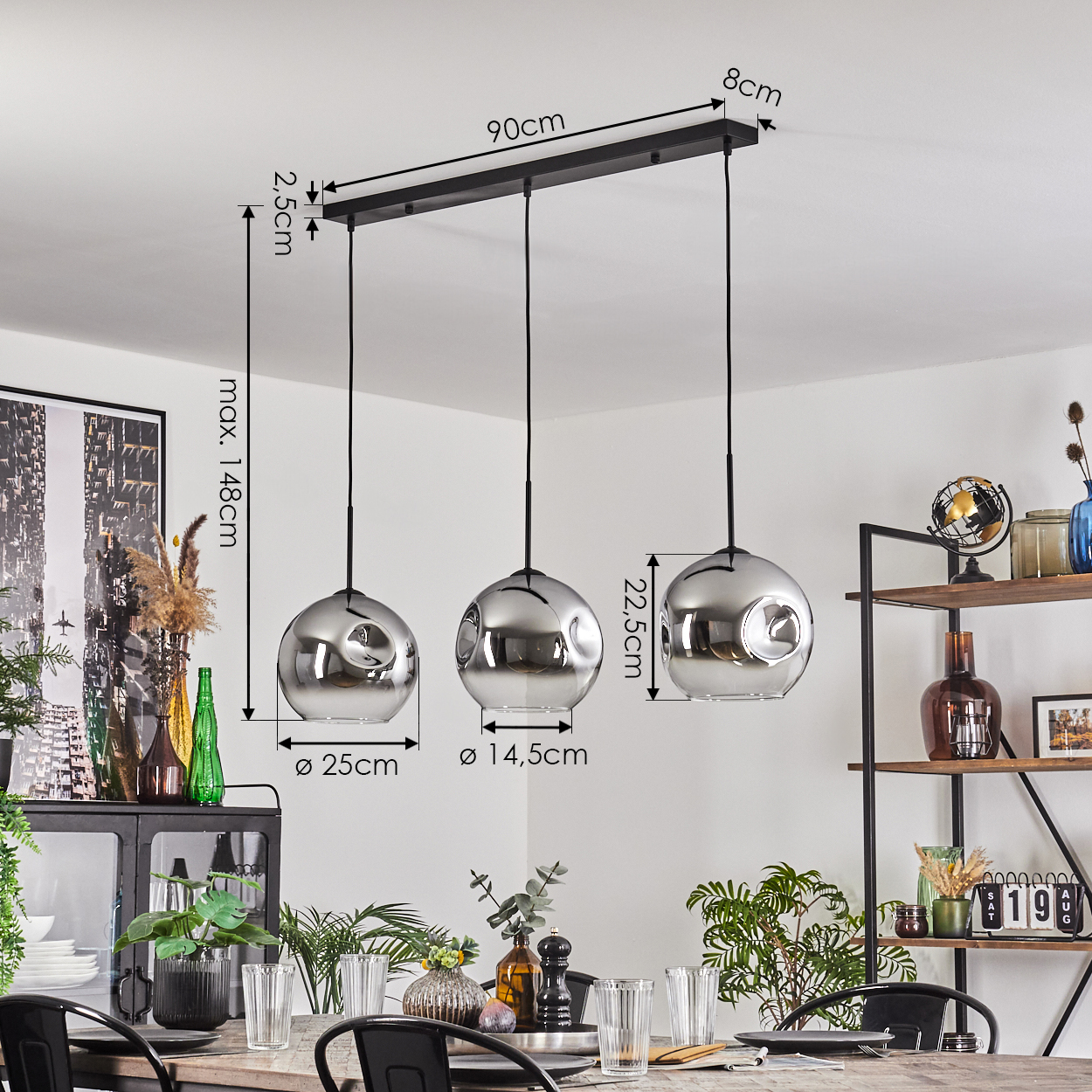 Drei Chrom-Pendelleuchten hängen über einem Esstisch mit Pflanzen. Maße sind angezeigt. Im Hintergrund ist ein Regal zu sehen.