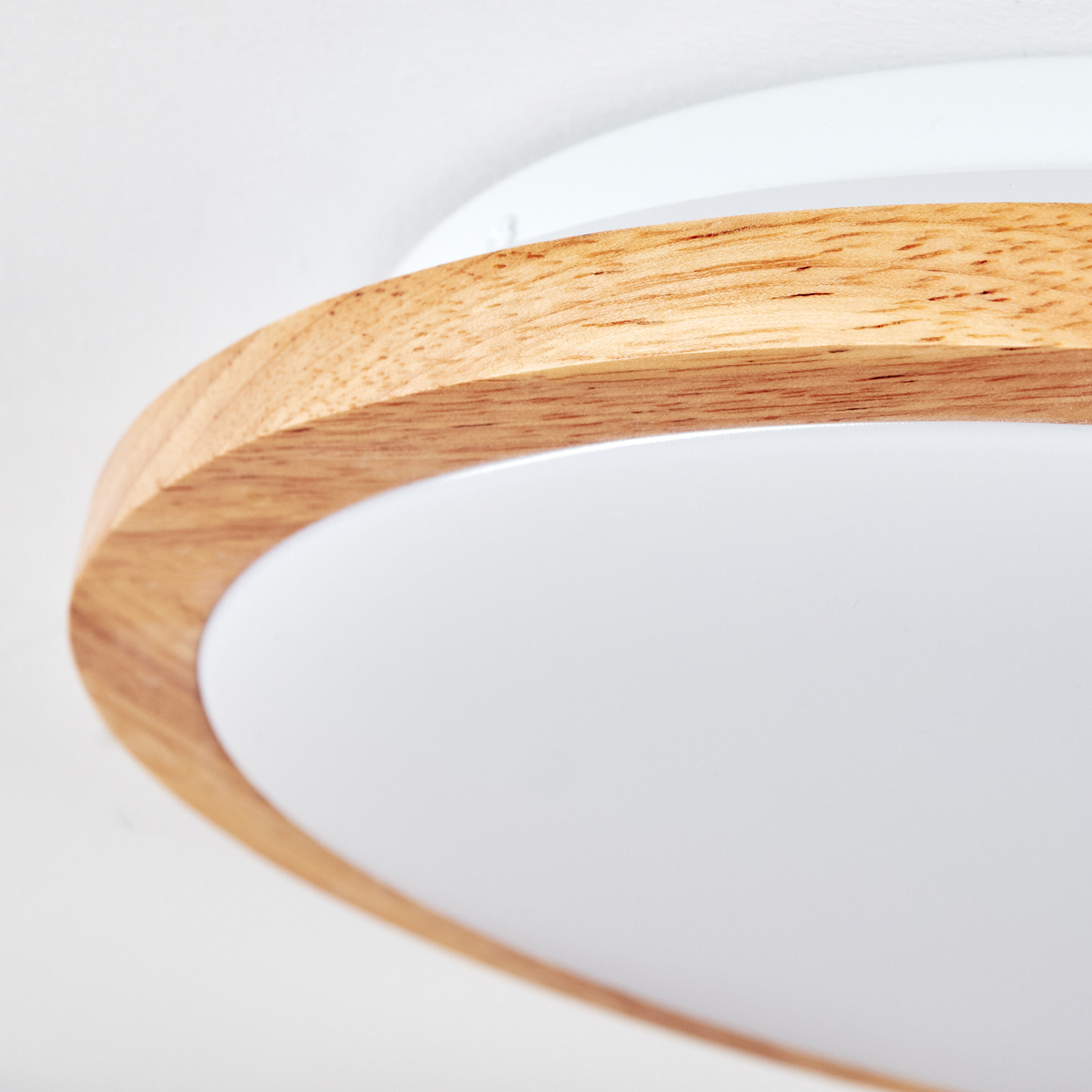 Nahaufnahme einer Deckenleuchte. Sie hat einen Holzrahmen, einen weißen Innenring und einen weißen Hintergrund. Das Licht ist eingeschaltet.