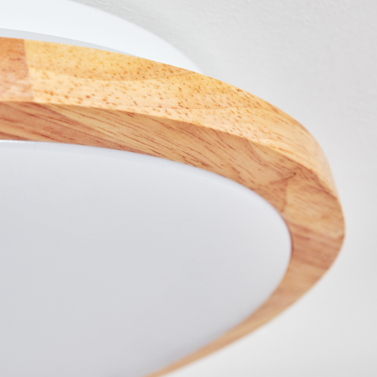 Nahaufnahme einer Deckenleuchte. Sie hat einen Holzrahmen und einen weißen, abgerundeten Diffusor. Der Hintergrund ist weiß.