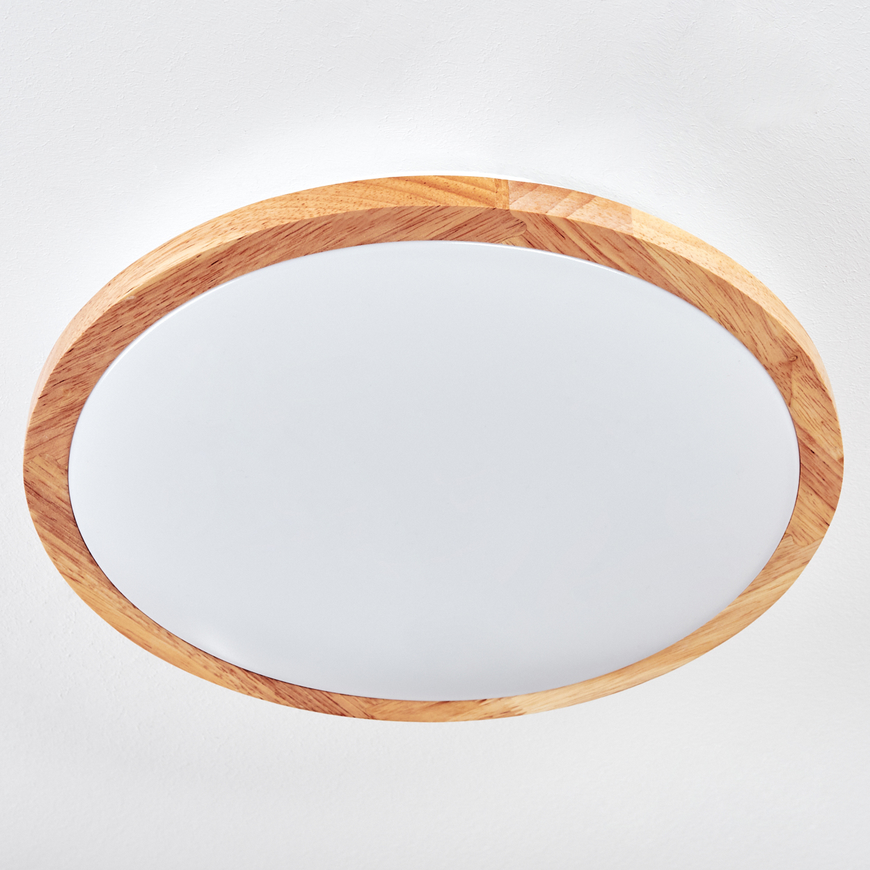 Eine ovale Deckenleuchte mit Holzrahmen. Die Mitte ist eine weiße, beleuchtete Platte. Der Hintergrund ist eine weiße Wand.