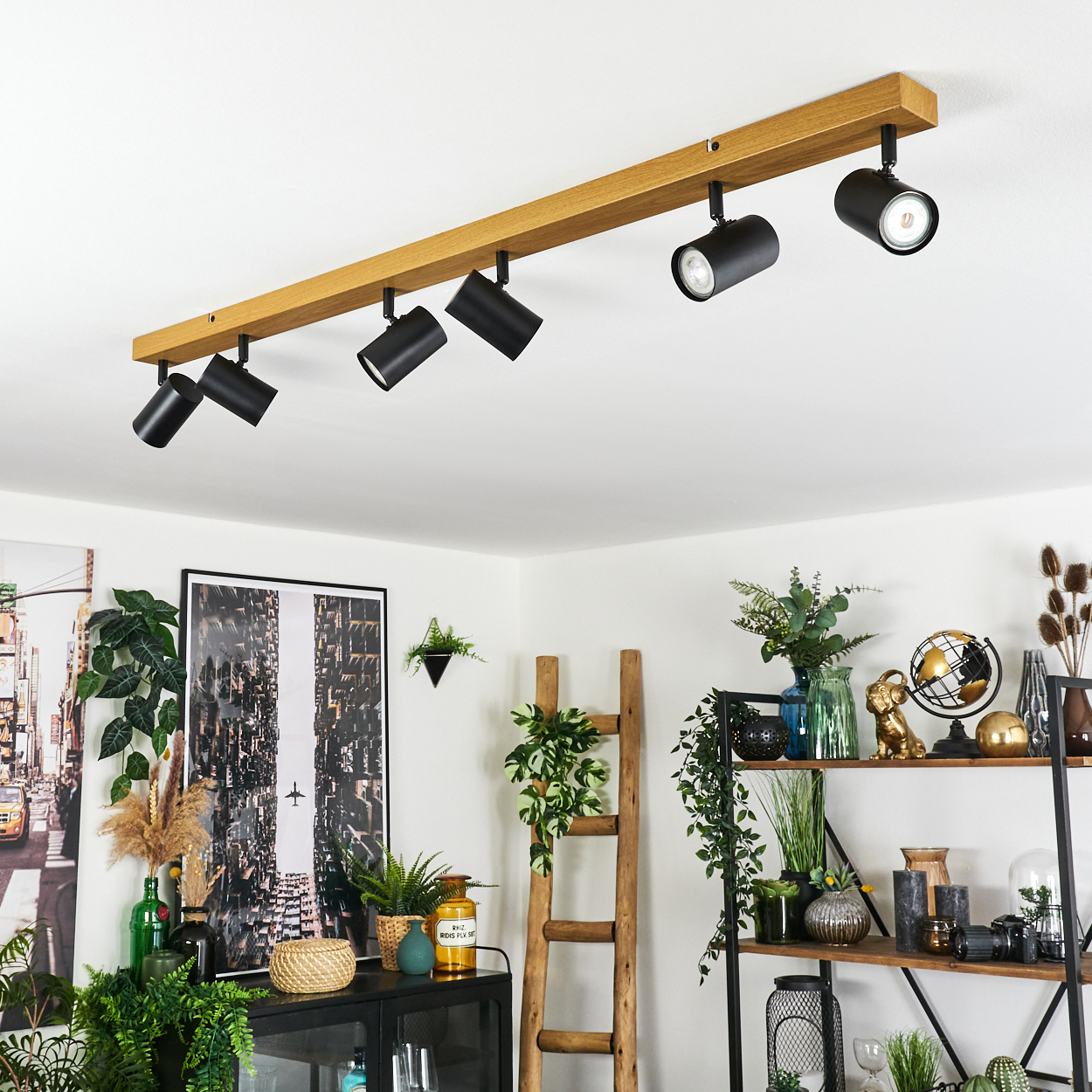 Ein modernes Interieur mit einer Deckenleuchte aus Holzbalken und verschiedenen dekorativen Elementen, darunter Pflanzen, eine Leiter und ein gerahmtes Bild.