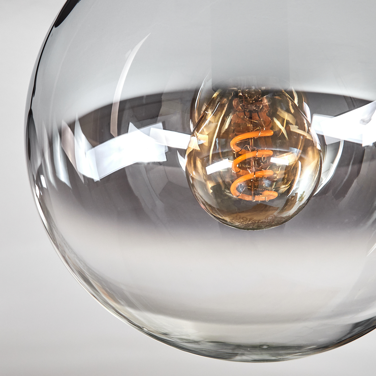 Nahaufnahme einer Glasleuchte. Eine warm getönte Glühbirne befindet sich in der transparenten Glaskugel.