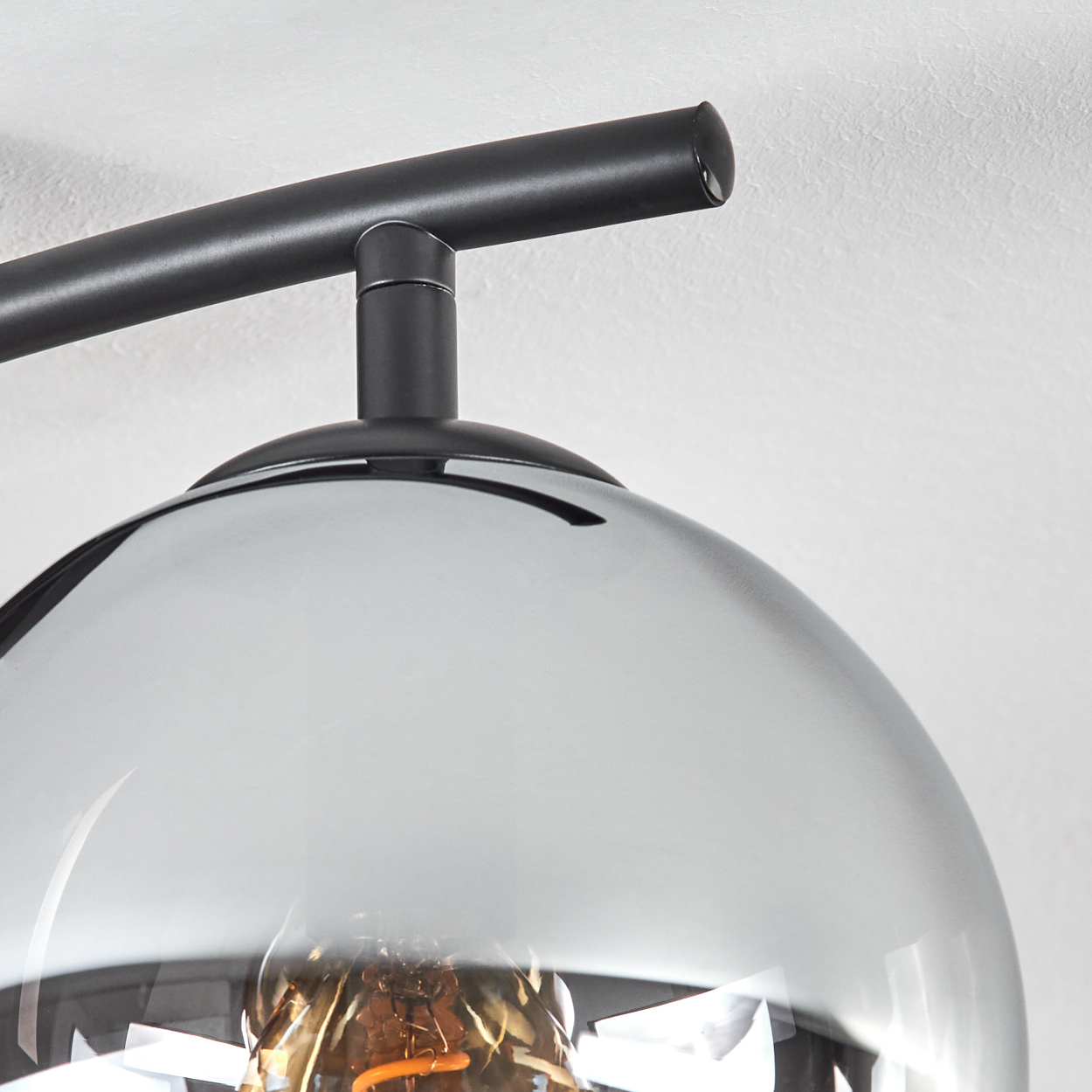 Nahaufnahme einer modernen Lampe. Sie hat einen Rauchglasschirm, einen schwarzen Metallrahmen und eine sichtbare Glühbirne. Vor einer weißen Wand.