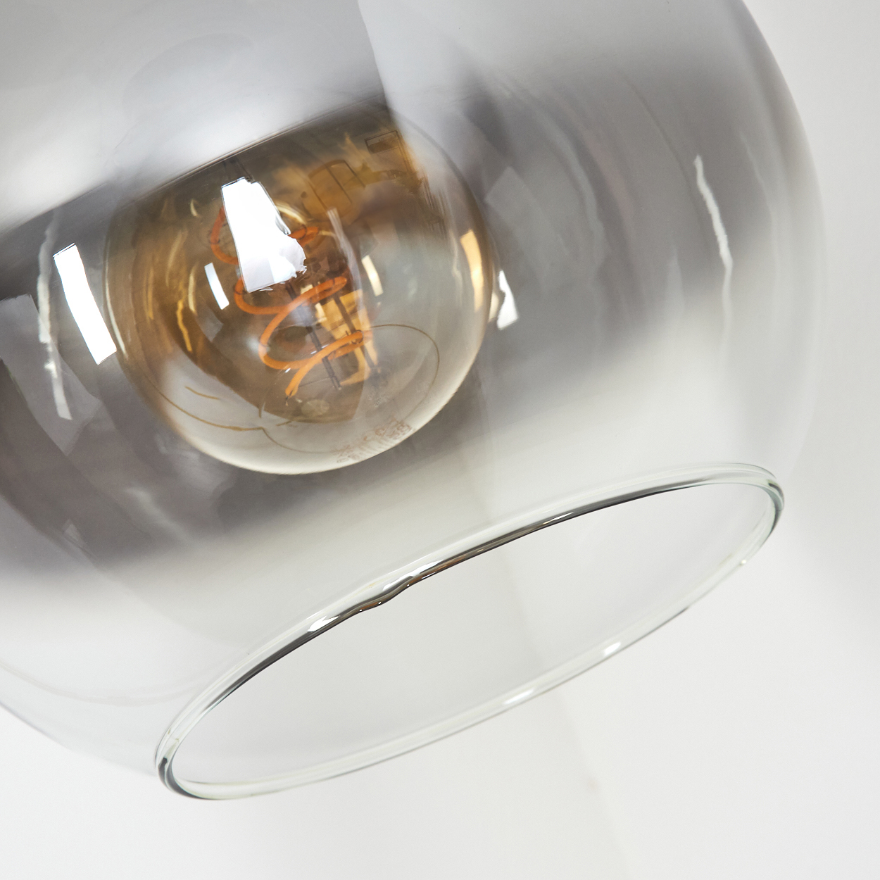 Nahaufnahme einer Glas-Pendelleuchte. Im Inneren ist eine warme Glühbirne sichtbar. Das Glas der Lampe hat einen Farbverlauf.