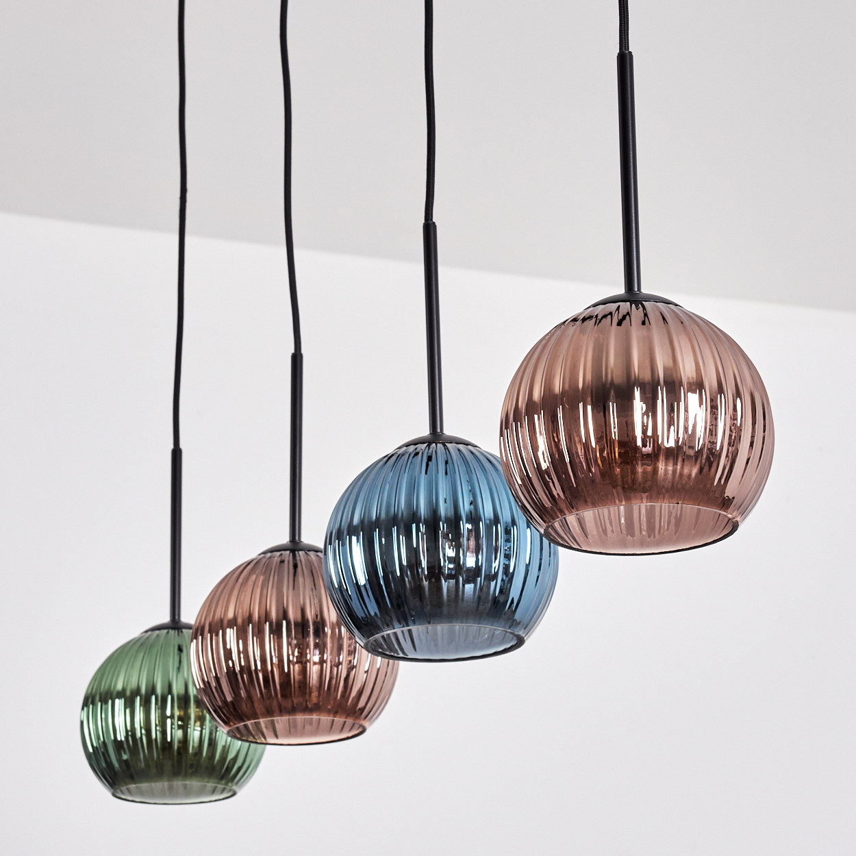 Vier bunte Pendelleuchten hängen von der Decke. Jede hat einen runden, geriffelten Glasschirm in verschiedenen Farben.