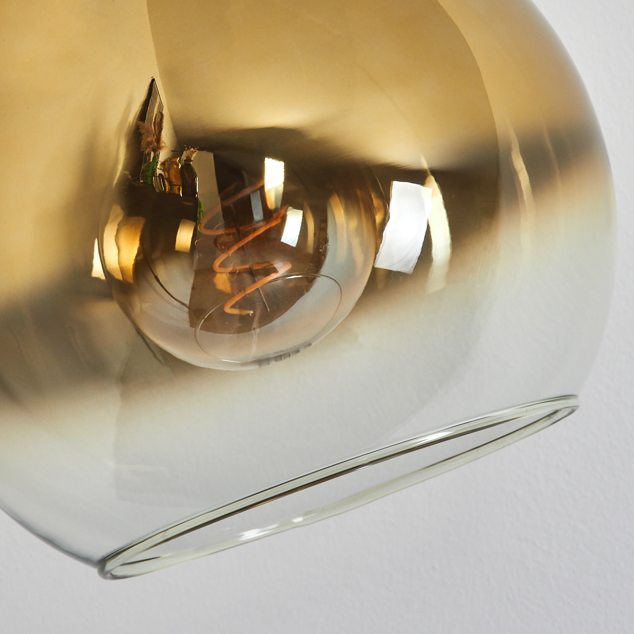 Nahaufnahme einer Glasleuchte mit einer Glühbirne im Inneren. Das Glas ist bernsteinfarben, der Hintergrund ist eine weiße Wand.