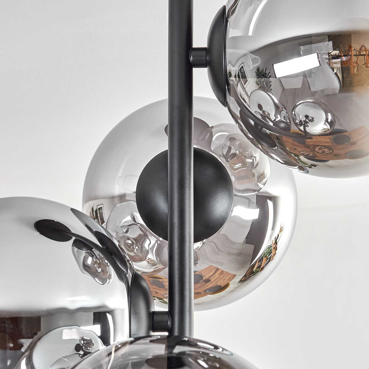 Nahaufnahme einer modernen Pendelleuchte mit mehreren kugelförmigen Glasschirmen in Silber und schwarzem Metallrahmen.