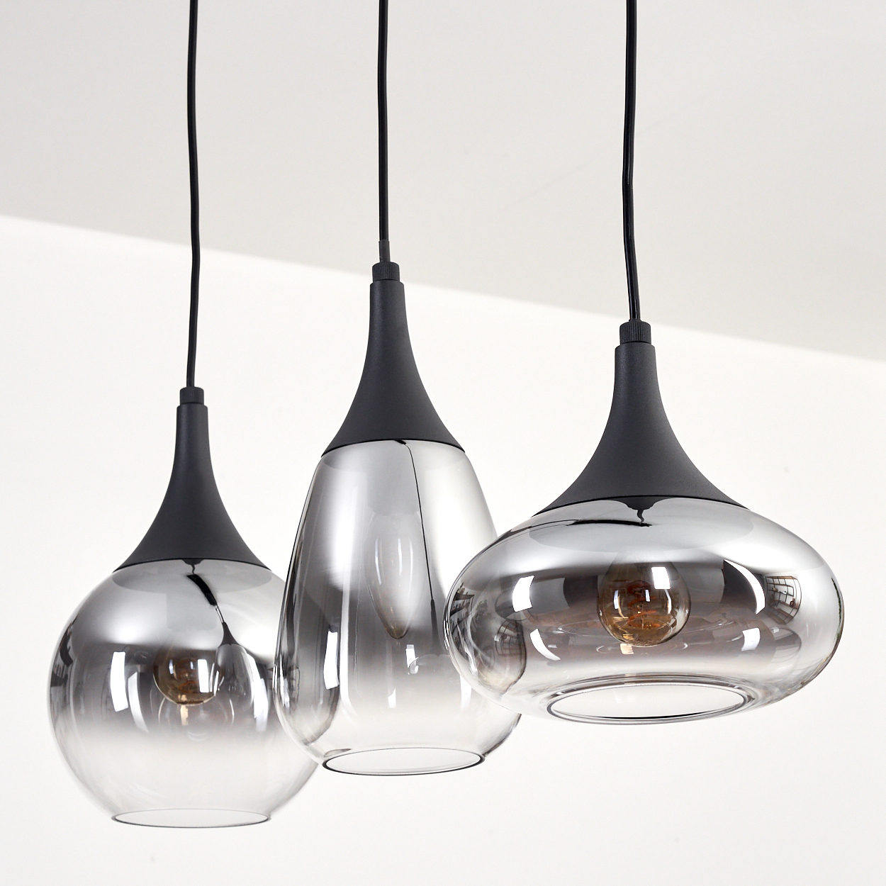 Drei Pendelleuchten mit Glasschirmen und schwarzen Oberteilen hängen von der Decke. Die Schirme reflektieren die Umgebung.