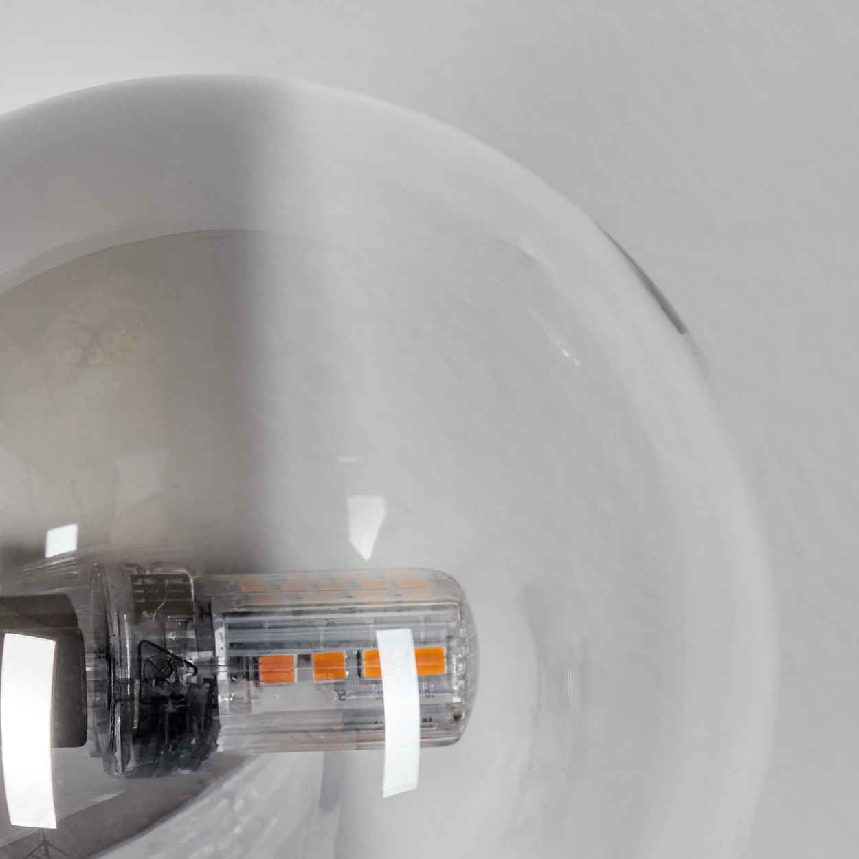 Nahaufnahme einer Glühbirne. Transparente Kunststoffkomponente mit orangefarbenen Lichtern in einer großen, weißen Glaskugel.