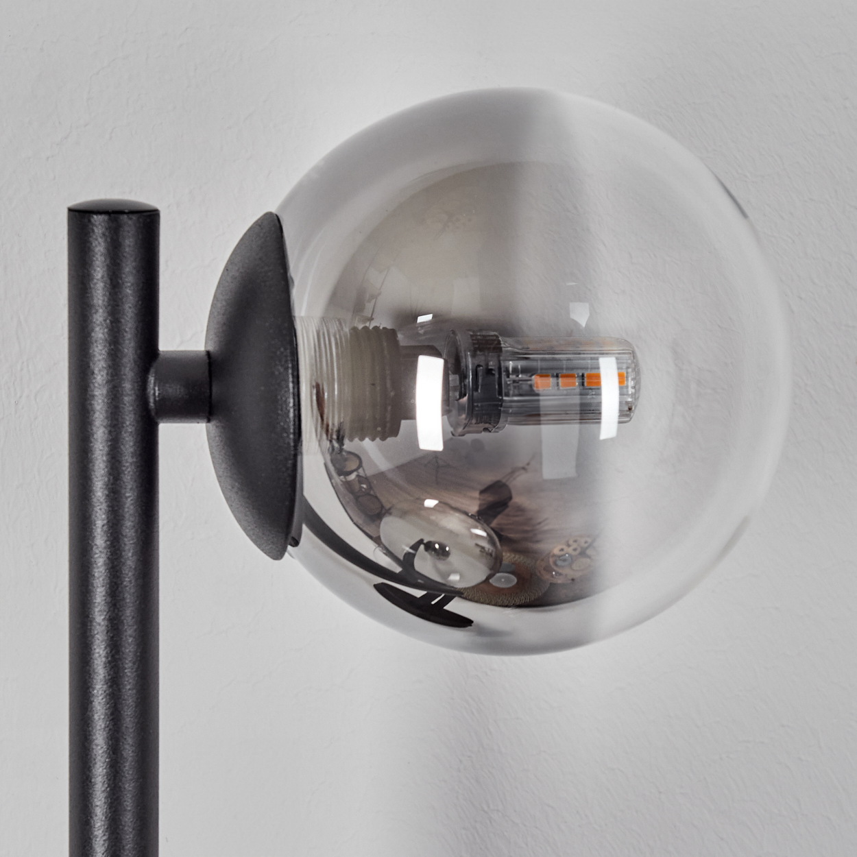 Eine moderne Lampe mit schwarzem Metallarm und rundem, rauchigem Glasschirm. Die Lichtquelle ist im Globus sichtbar.