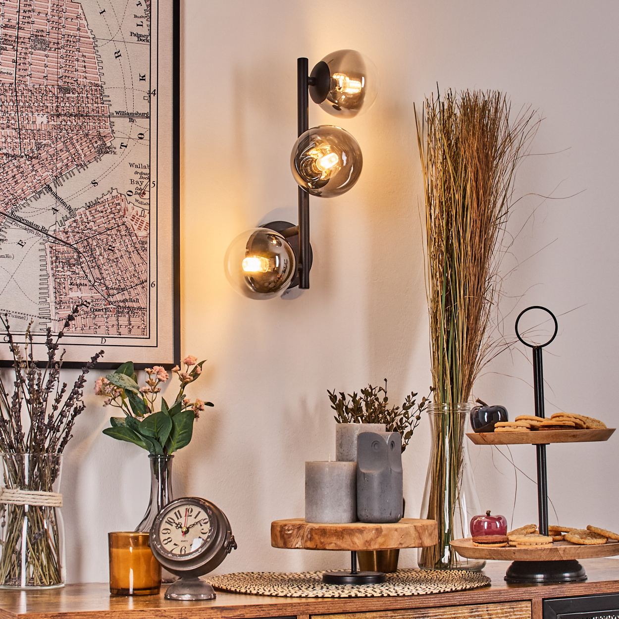 Ein Raum mit Karte, moderner Lampe, Blumen, Kerzen, Uhr und zweistöckigem Tablett mit Keksen und einem Deko-Apfel.