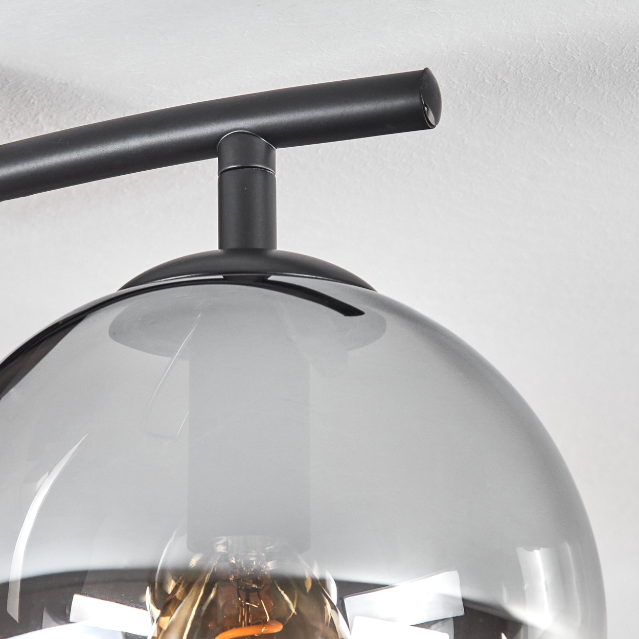 Nahaufnahme einer schwarzen Lampe mit grauem Glasschirm. Eine Glühbirne ist sichtbar. Der Hintergrund ist weiß.