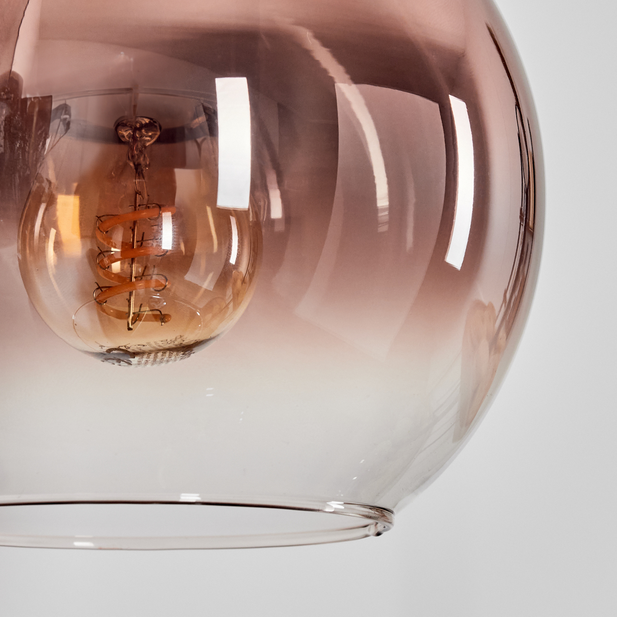 Nahaufnahme einer Glasleuchte mit Glühbirne. Das Glas ist braun getönt und reflektiert Licht. Der Hintergrund ist weiß.