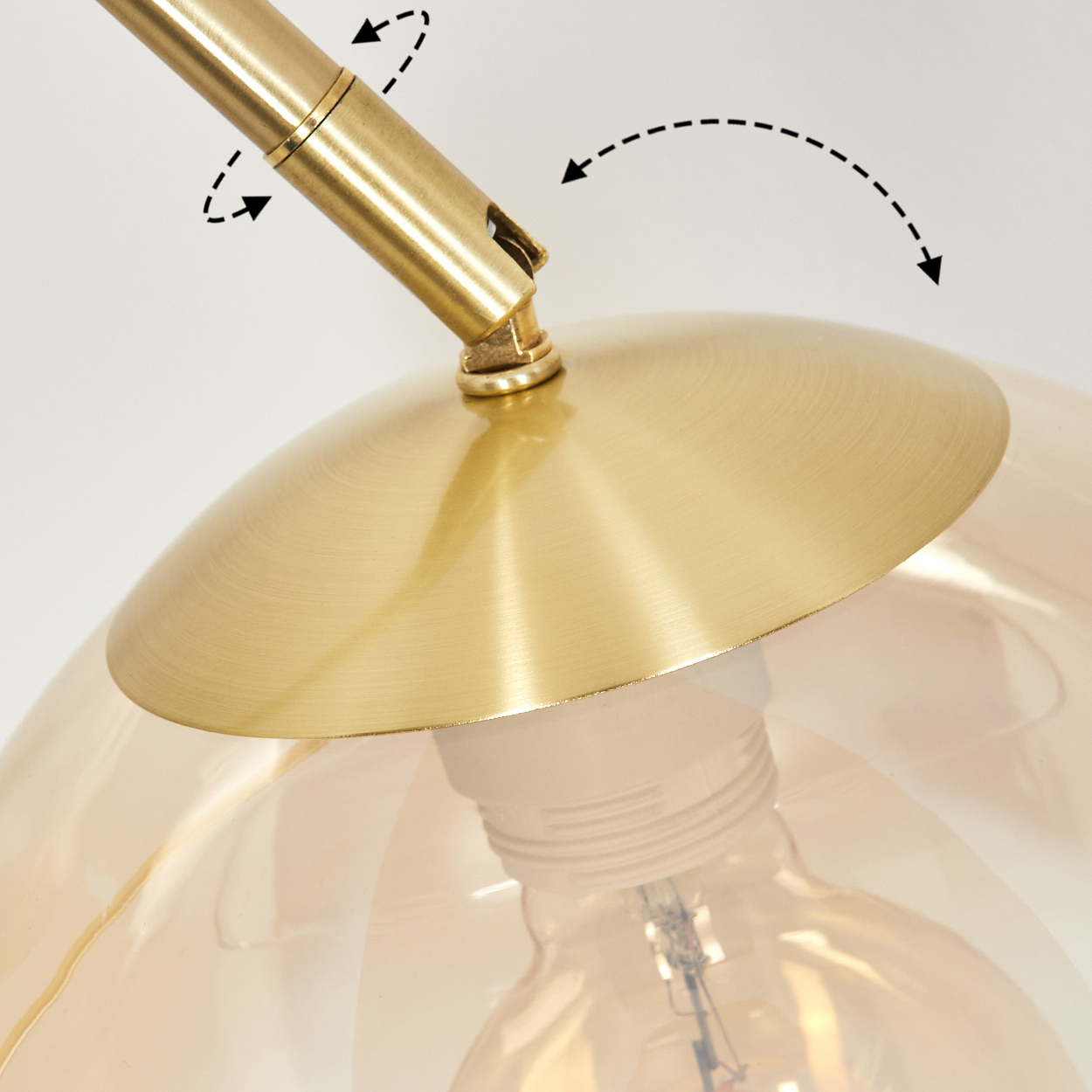 Nahaufnahme einer Messinglampe. Ein gebogener Arm verbindet sich mit einem kuppelförmigen Schirm. Eine Glühbirne ist durch das bernsteinfarbene Glas sichtbar.