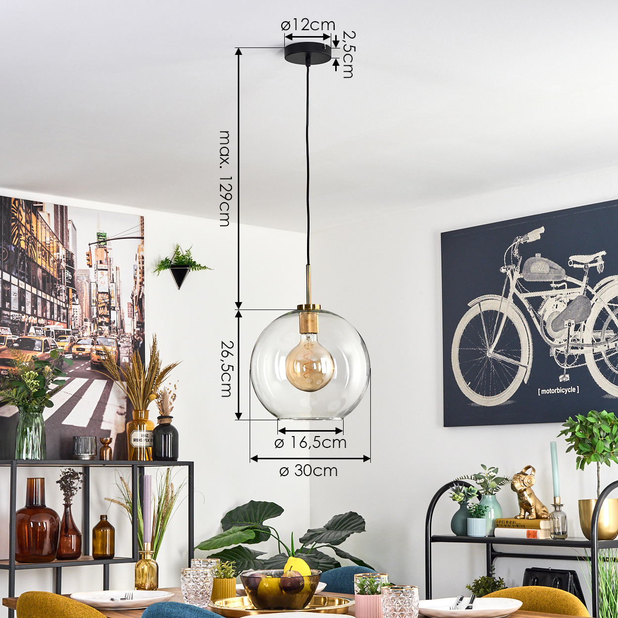 Ein modernes Esszimmer mit einer Glaskugel-Pendelleuchte. Kunstwerk einer Stadt und eines Fahrrads. Tisch mit Obst und Pflanzen.