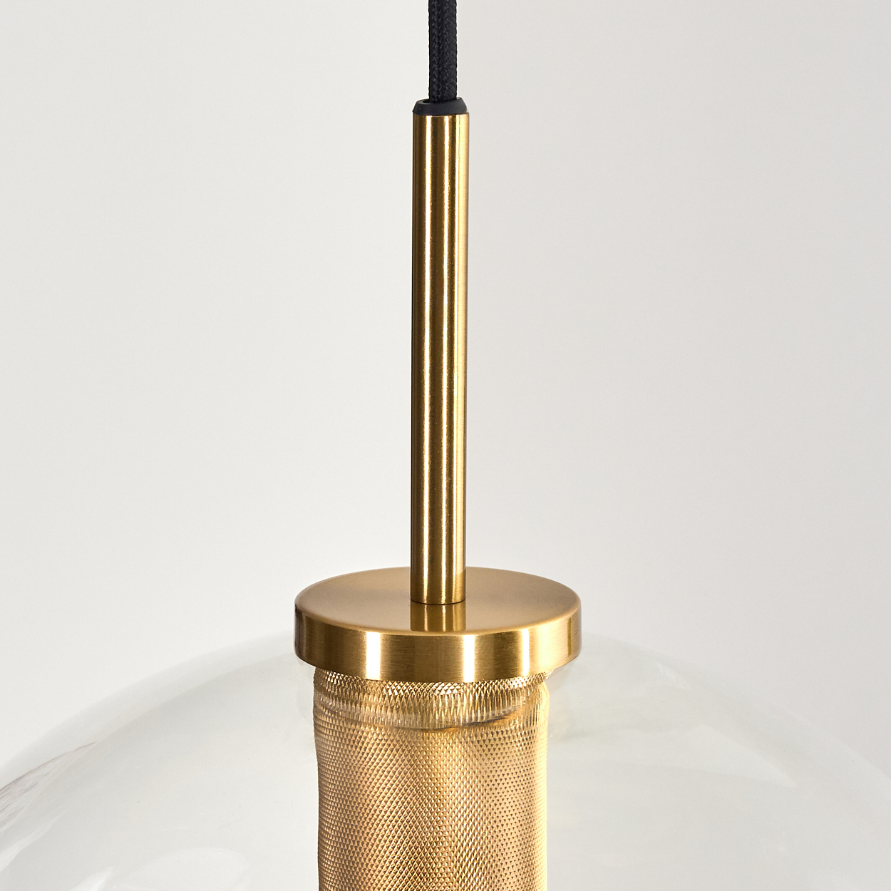 Nahaufnahme einer Pendelleuchte. Sie hat eine goldfarbene Metalloberfläche mit Glasschirm und schwarzem Kabel.