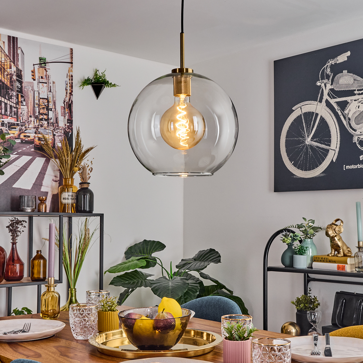 Ein Esszimmer mit Holztisch, Glaslampe und Obstschale. Kunstwerke an der Wand.