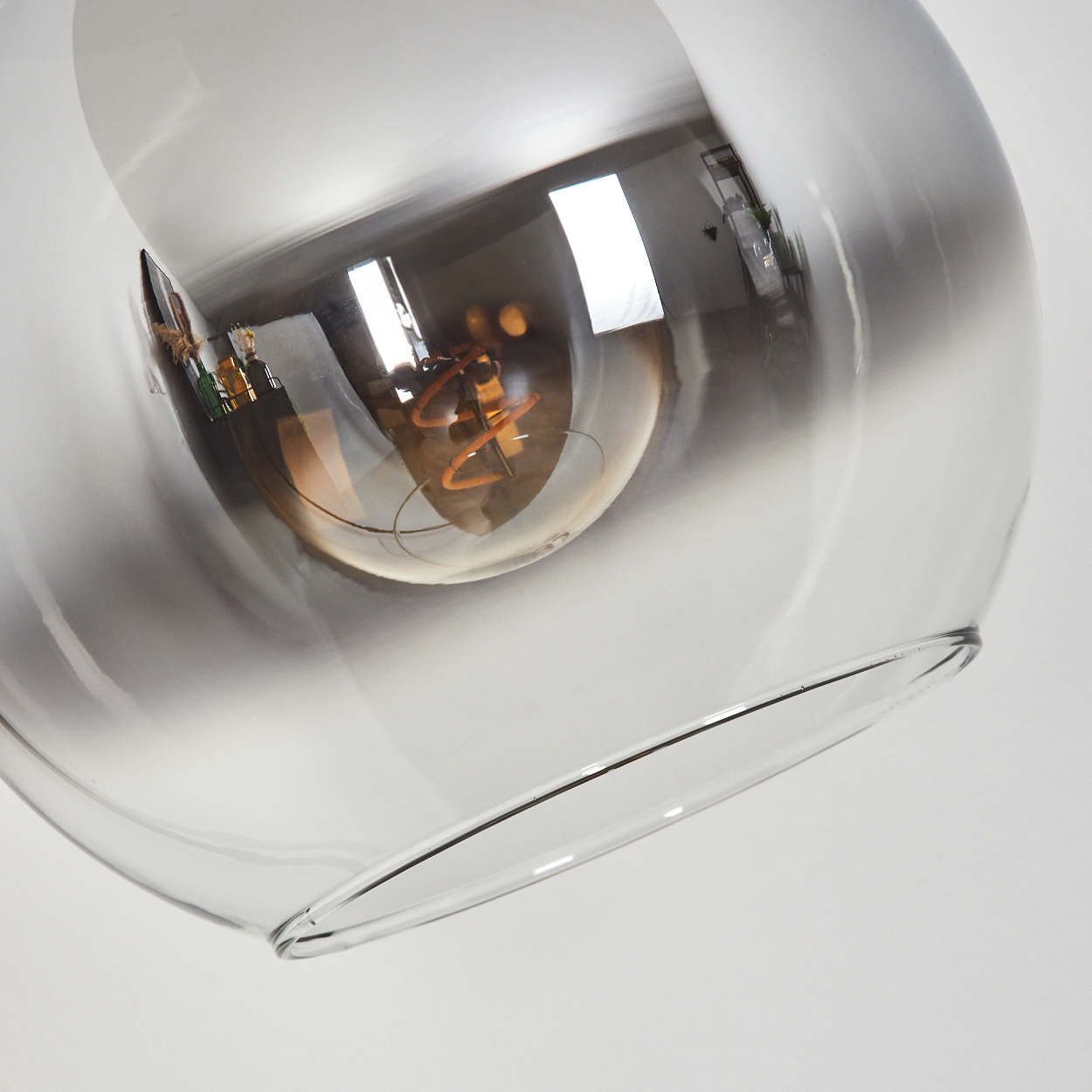 Eine klare Glaslampe mit einer sichtbaren Glühbirne. Die Lampe spiegelt den Raum mit Fenstern und Möbeln.