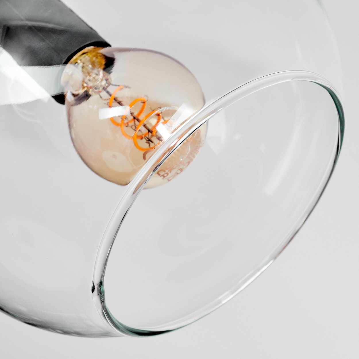 Nahaufnahme einer Leuchte mit Glasschirm und Glühbirne mit orangefarbenem Glühfaden. Der Hintergrund ist weiß.